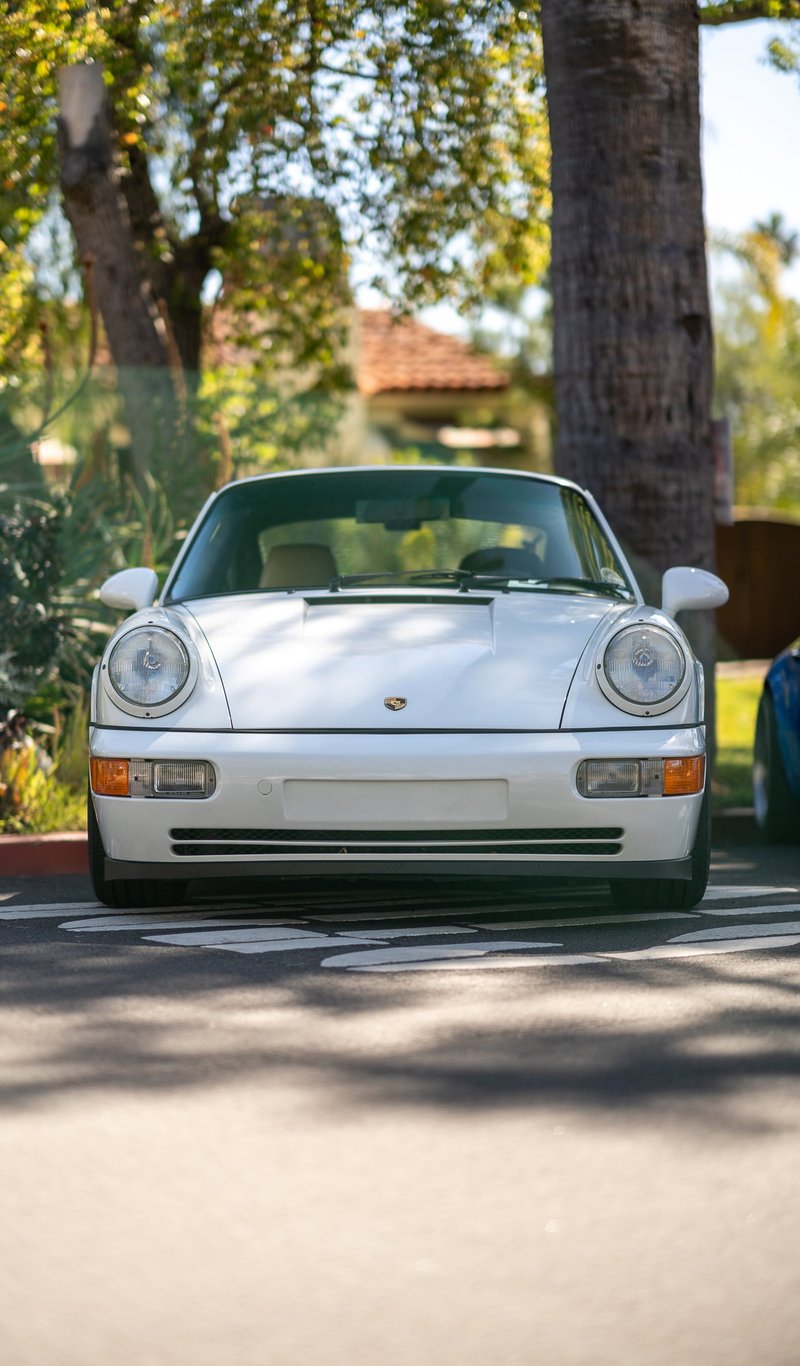 White Porsche 911 Carrera 4 (964) parked at a sunny outdoor car show.