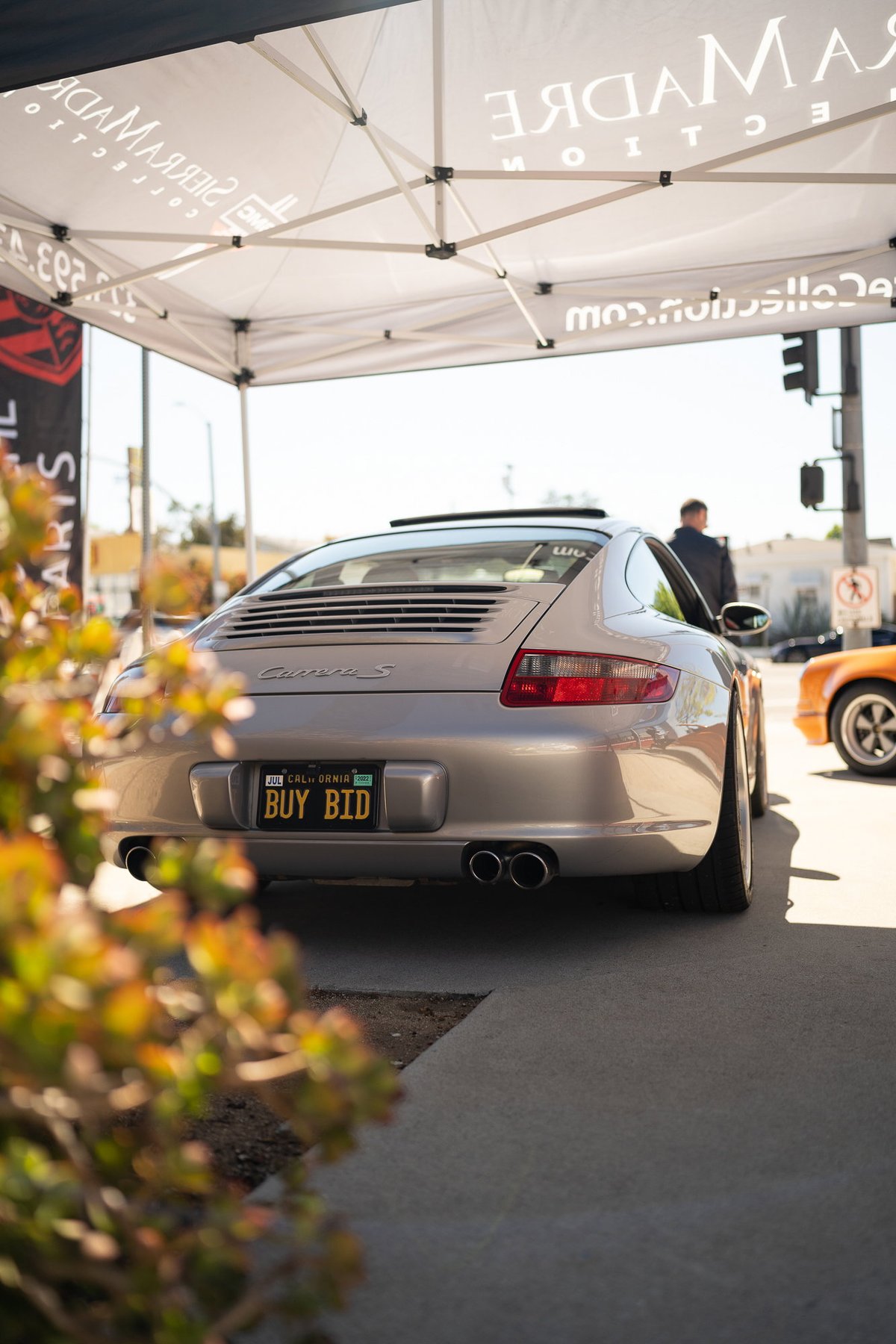Rear view of a silver Porsche 911 Carrera S with a "BUY BID" license plate.