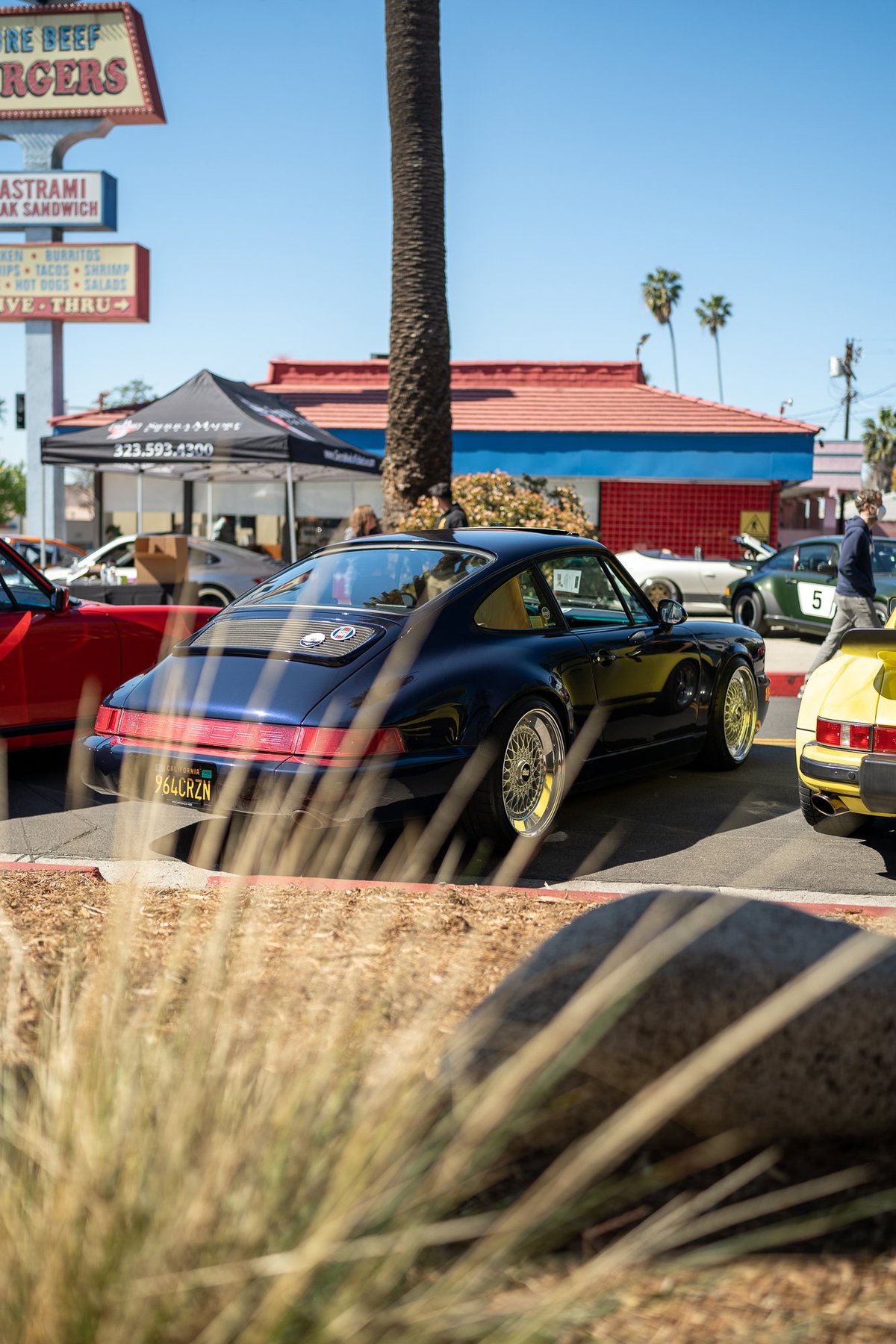 Dark blue Porsche 911 with gold mesh rims and yellow interior, parked at a car show.