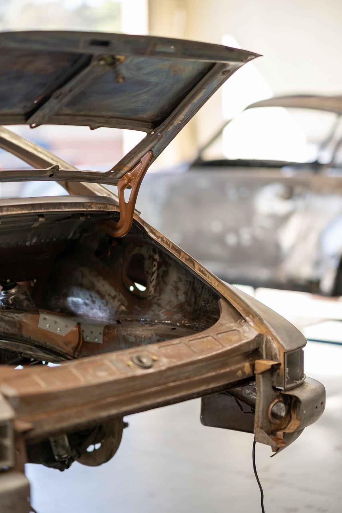 A rusty classic Porsche 911, front trunk open, undergoing restoration.