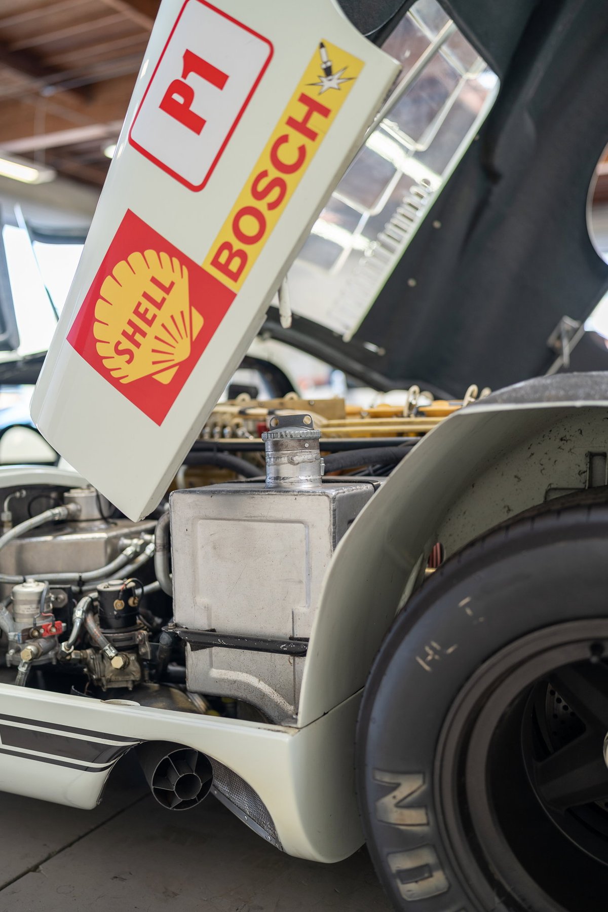 Vintage race car with "P1" and Shell/Bosch livery on open hood. Exposed engine bay, black rims, exhaust visible.