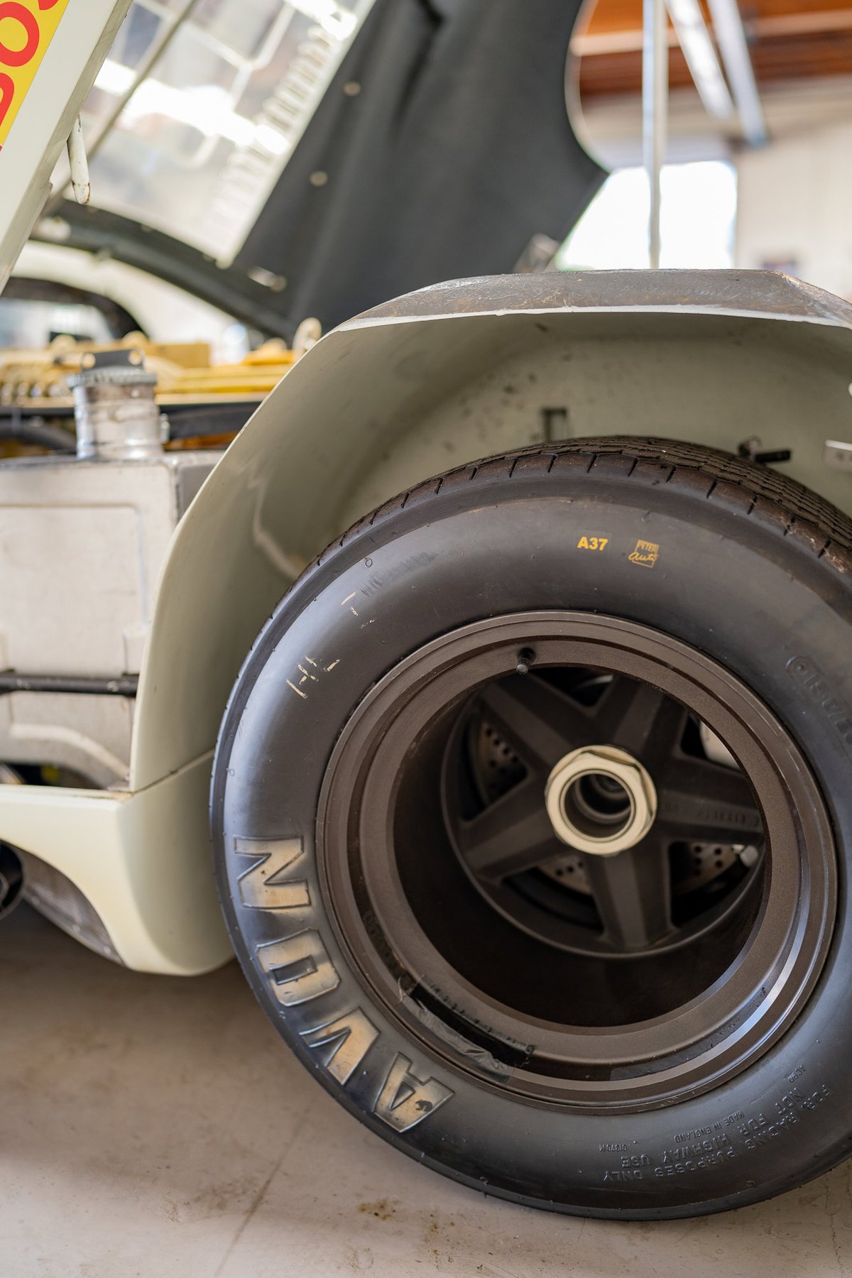Close-up of a classic race car's front tire and wheel. The Avon tire features gold lettering.