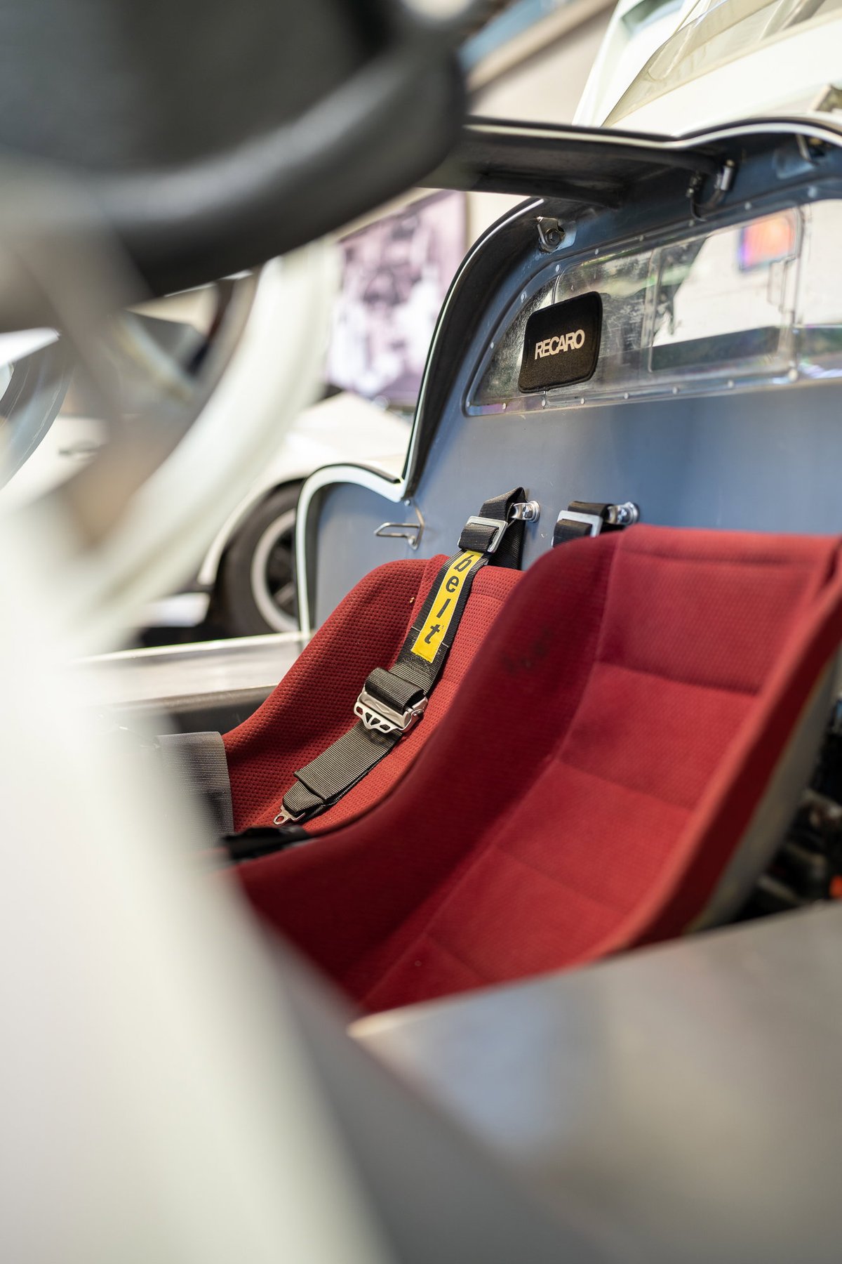 Red Recaro racing seats and harnesses in a silver classic sports car with "RECARO" branding.