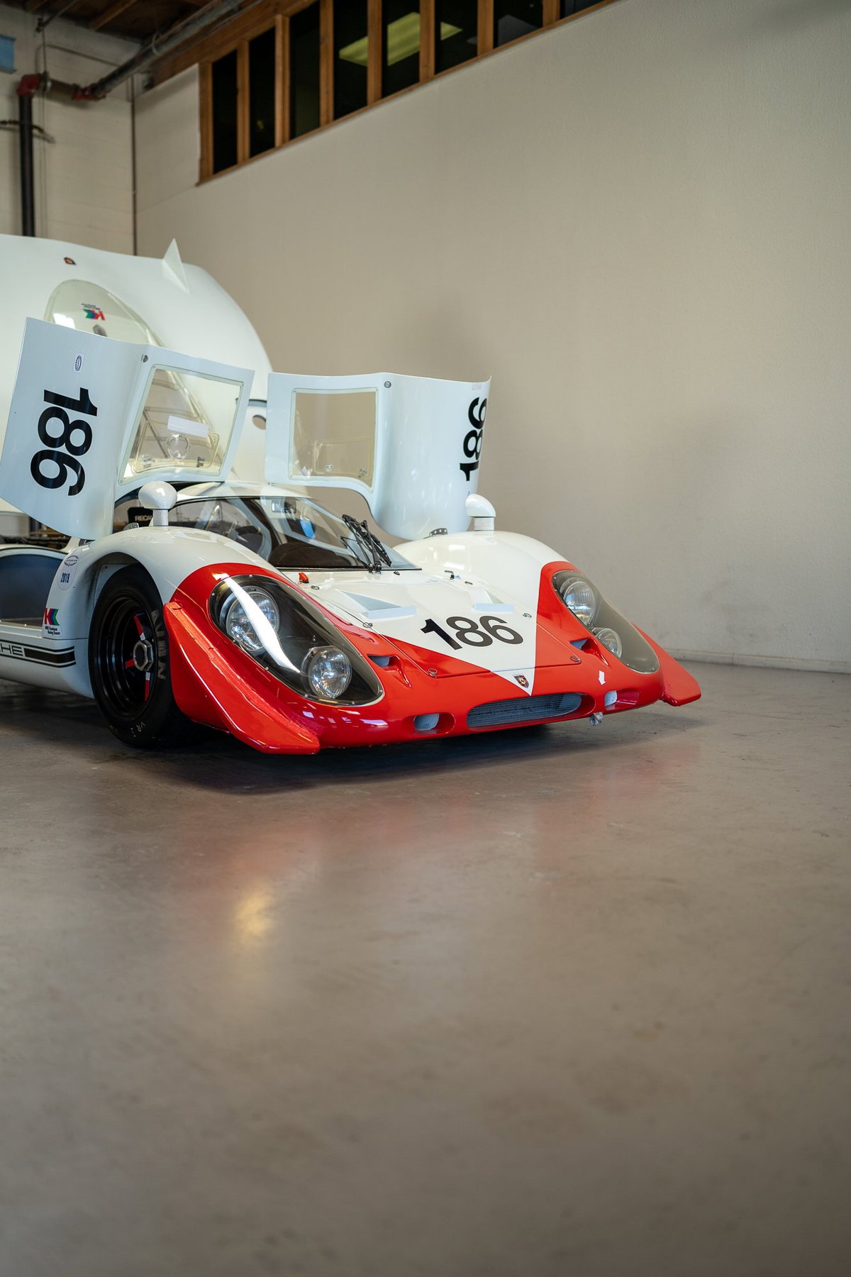 White Porsche 917 race car with red trim, number 186 livery, and gullwing doors open.