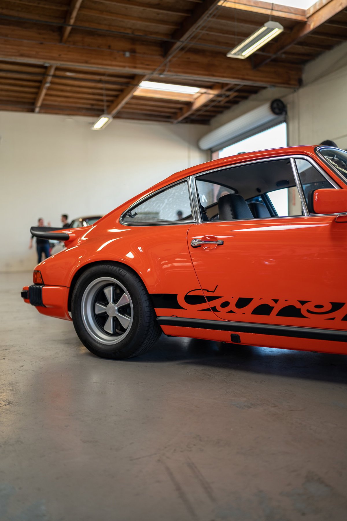 Orange Porsche 911 Carrera with black side livery and Fuchs rims.