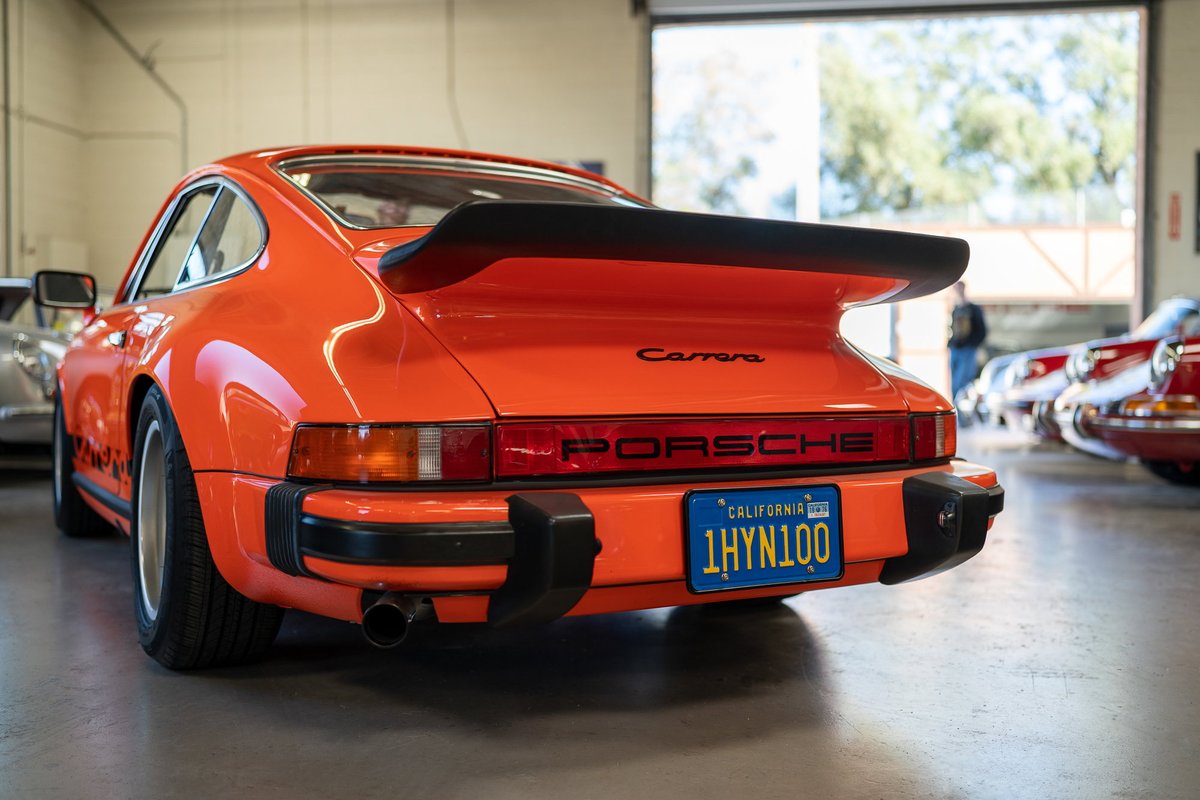 Orange 1970s Porsche 911 Carrera Targa with a black whale tail spoiler and black trim.