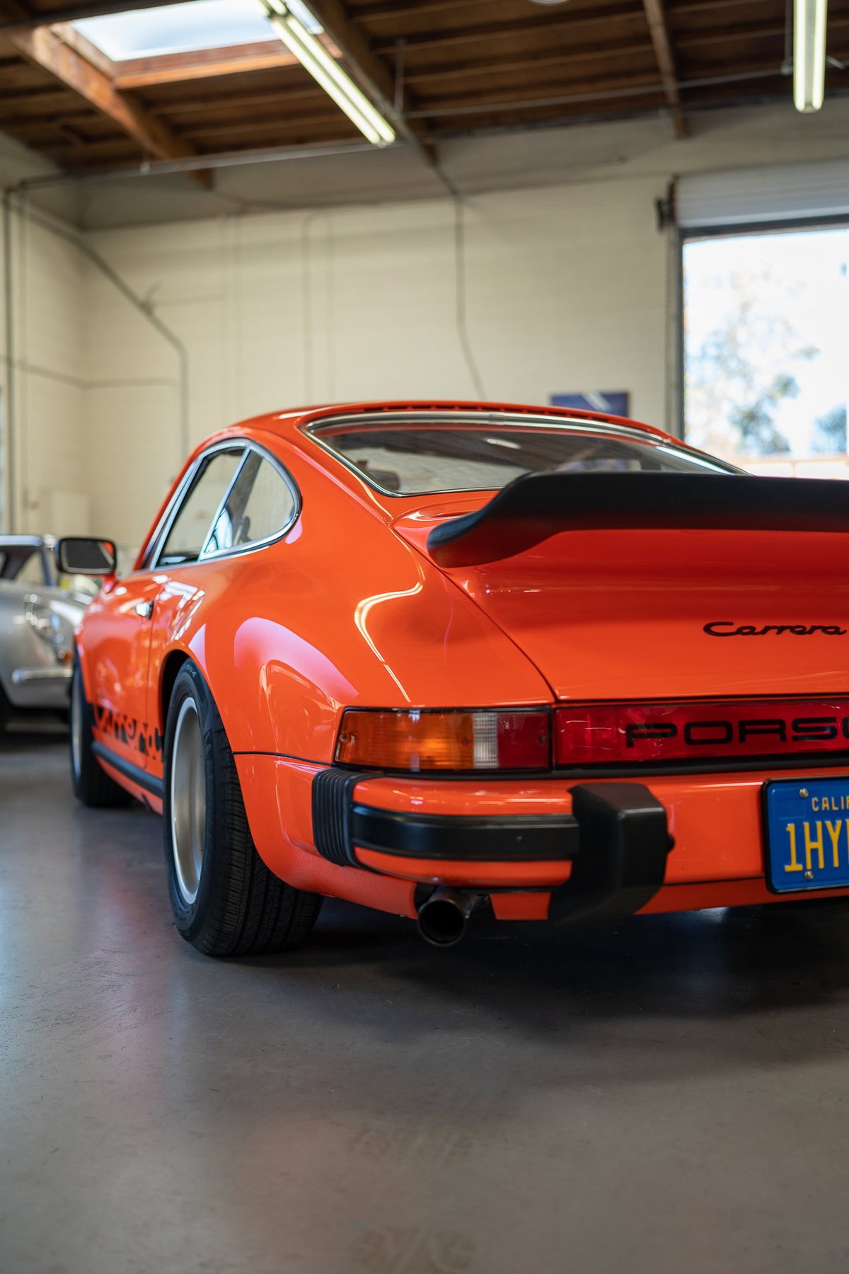 Orange 1980s Porsche 911 Carrera with black trim, spoiler, and livery.