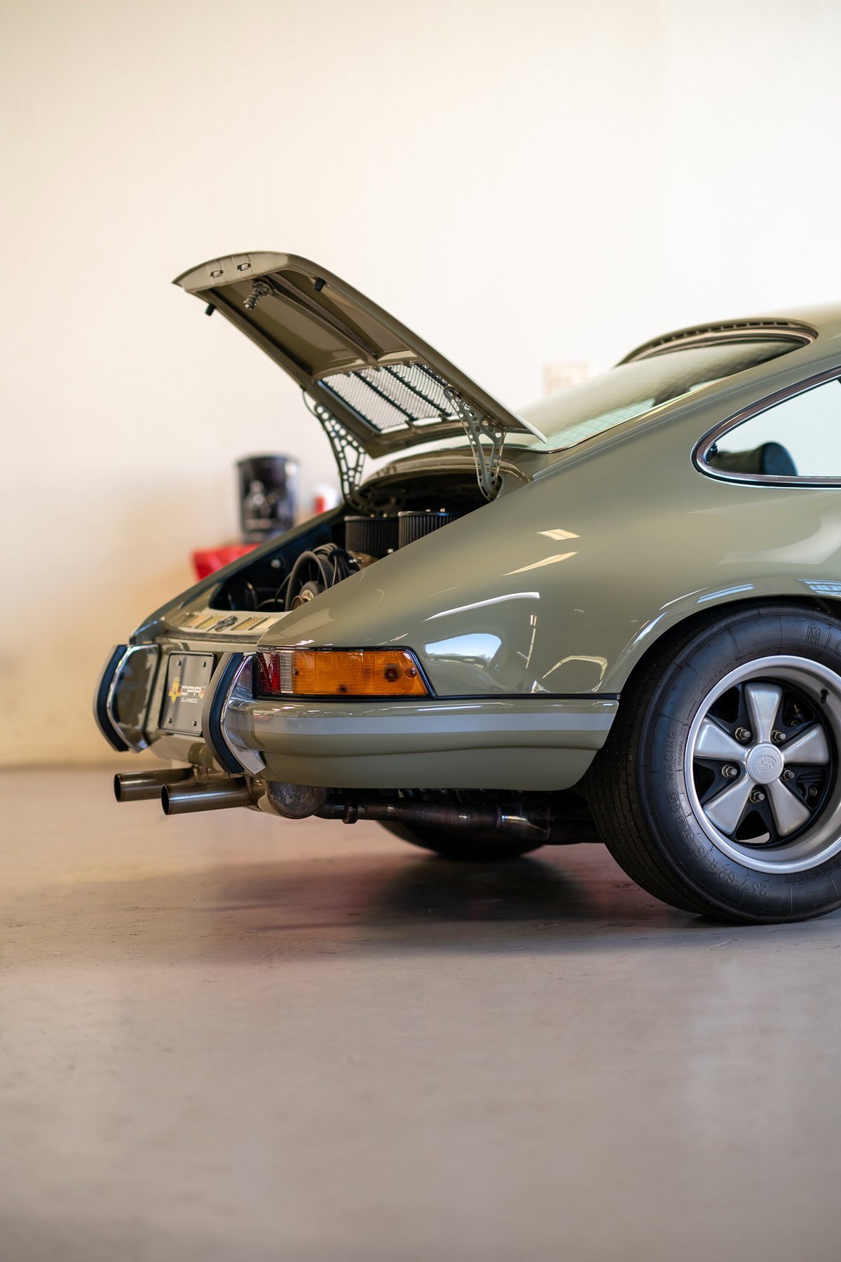Porsche 911 Targa engine bay open, showing off the flat-six engine. Olive green paint with chrome trim.