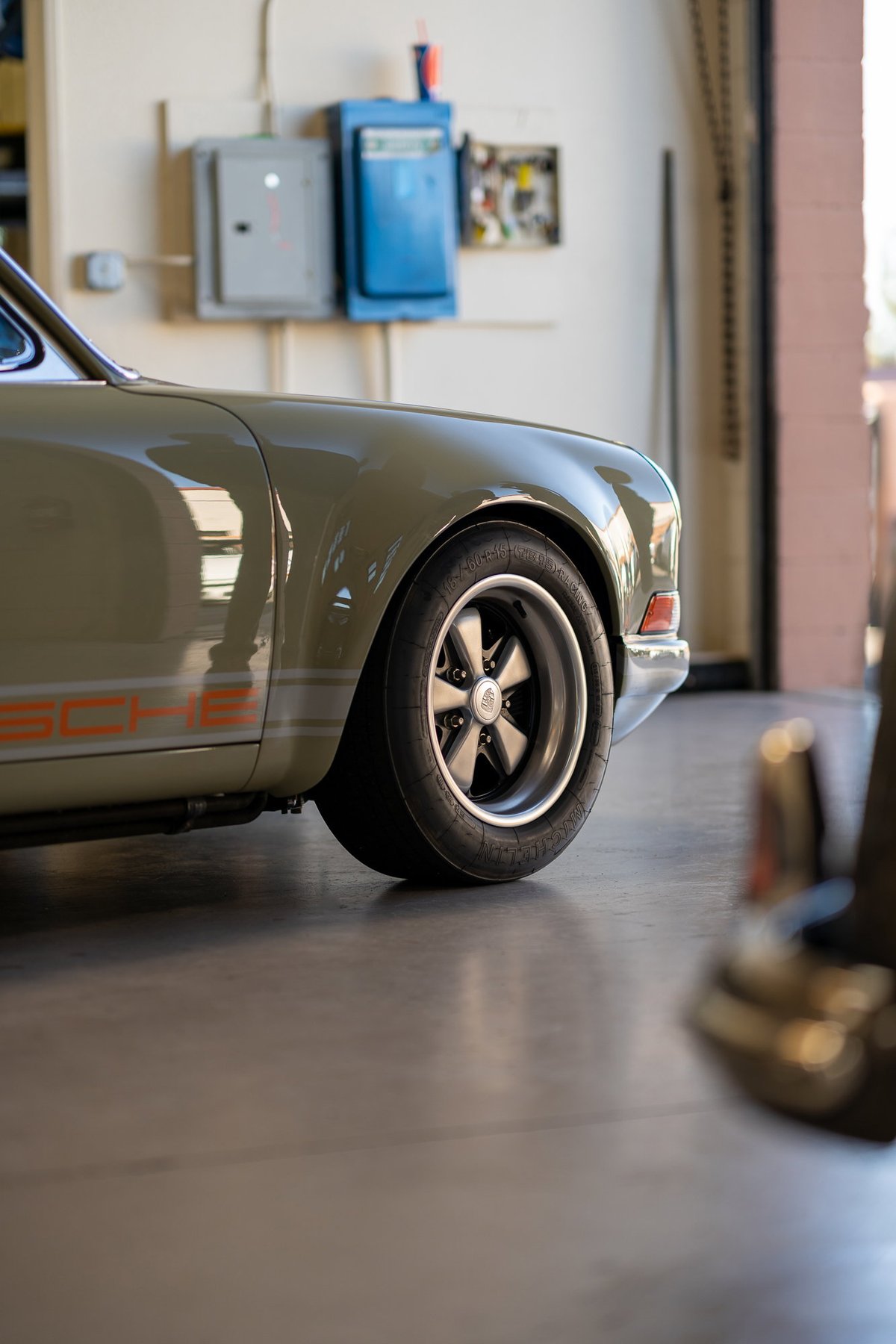 Close-up of a vintage Porsche 911 in olive green with orange livery, showing its Fuchs wheels.
