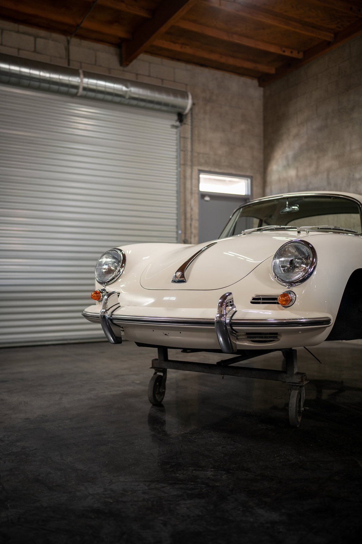 Close-up of a white Porsche 356 front end on a dolly in a garage setting.