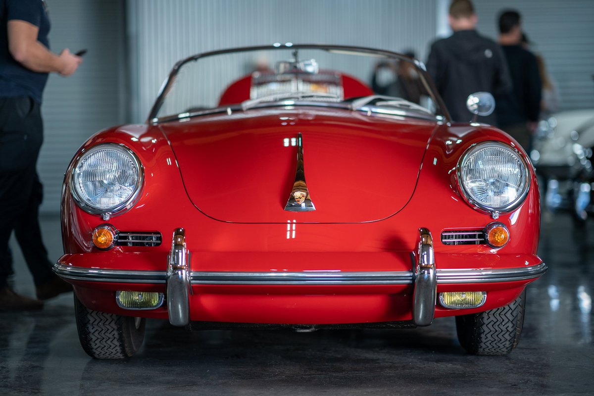 Front view of a red 1950s Porsche 356 Speedster with chrome trim and headlights.