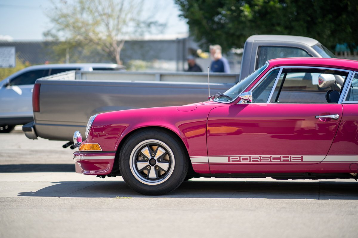 Pink Porsche 911 with silver side livery and Fuchs wheels parked outdoors.
