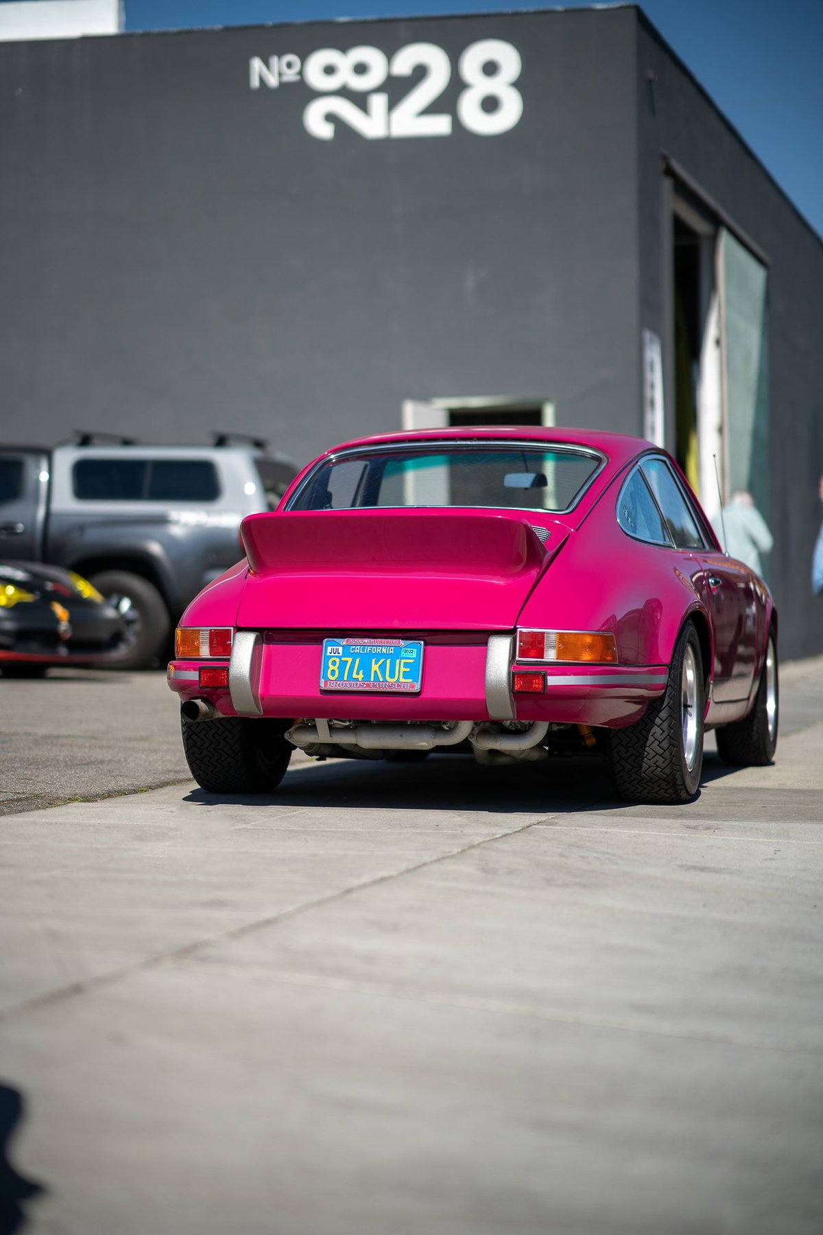 Rear view of a bright pink Porsche 911 with silver trim and Fuchs rims.