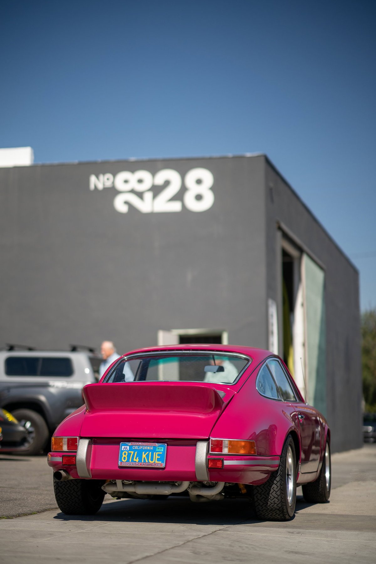 Rear view of a pink 1970s Porsche 911 with a ducktail spoiler and chrome trim.