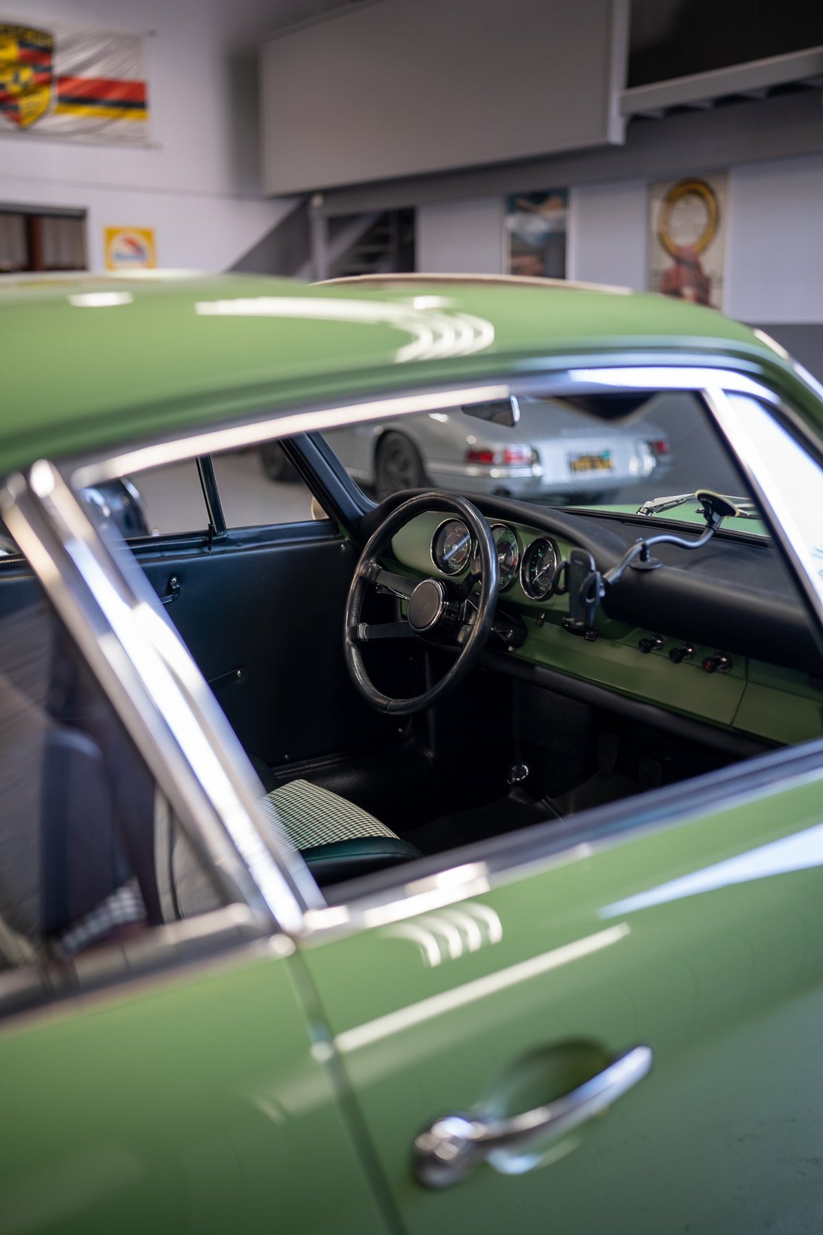 1960s Porsche 356 interior and green exterior. The car has a classic steering wheel and gauge cluster.