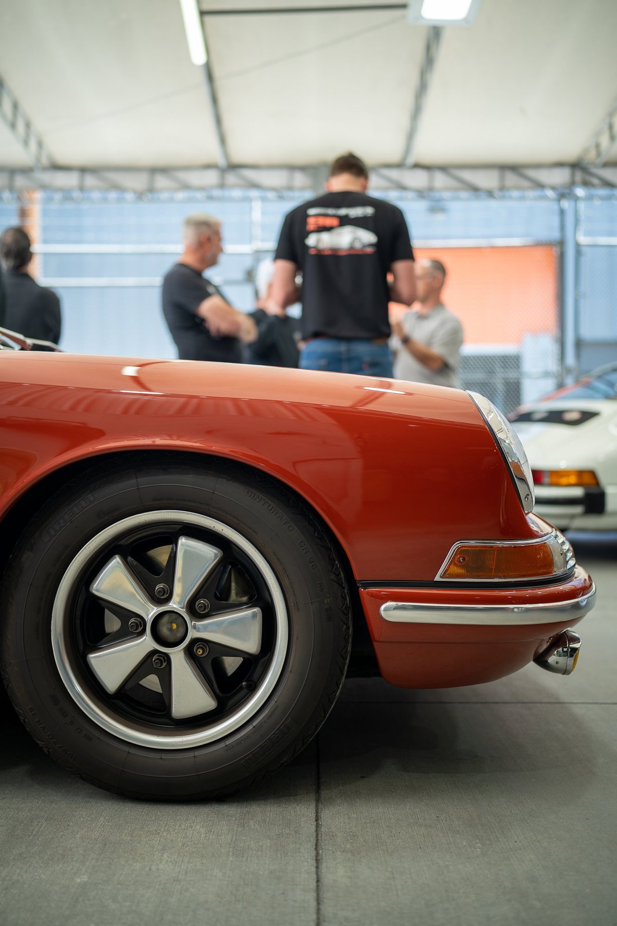 Red 1970s Porsche 911 with silver Fuchs rims and chrome trim.