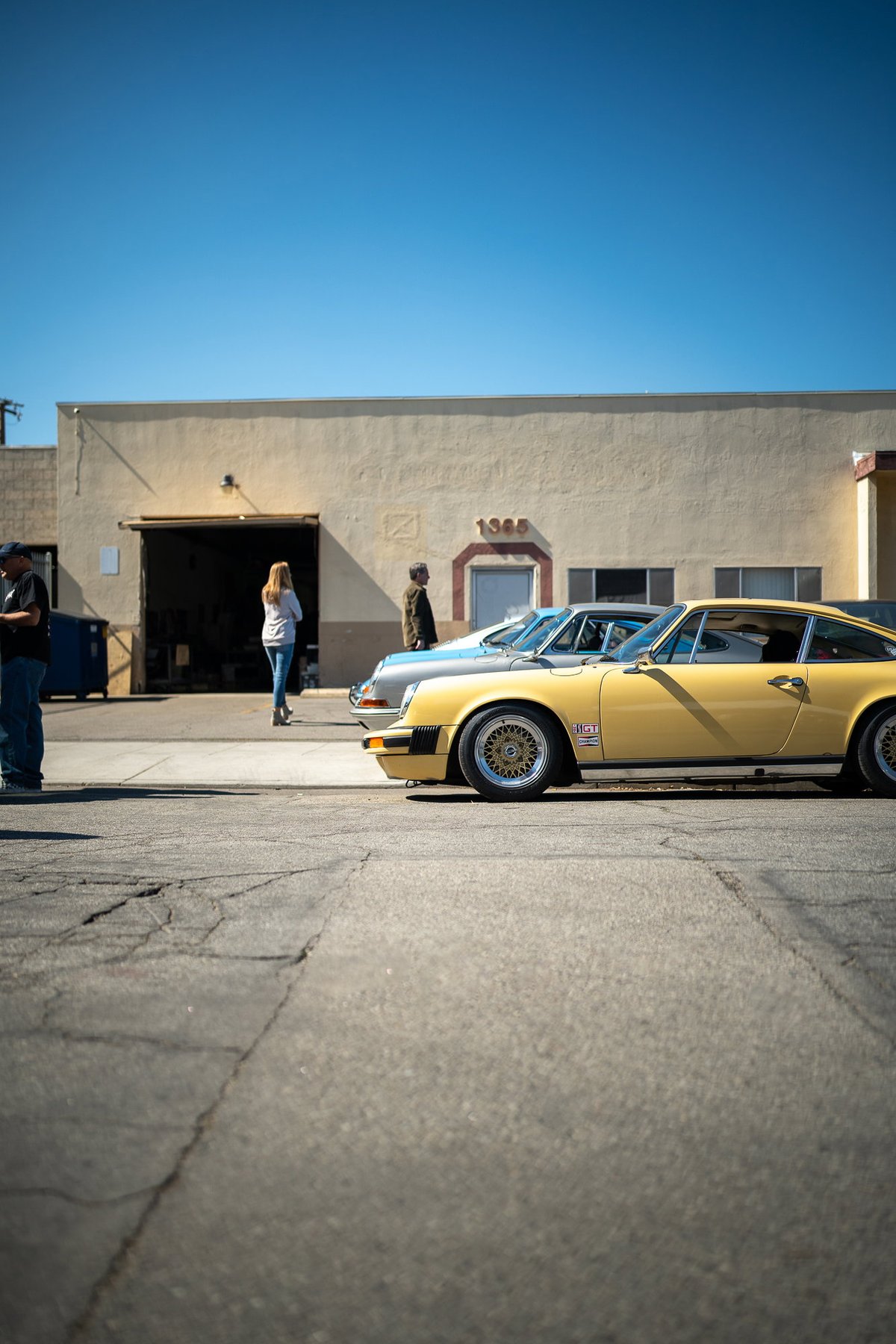 Yellow Porsche 911 with gold mesh rims parked outside a building.