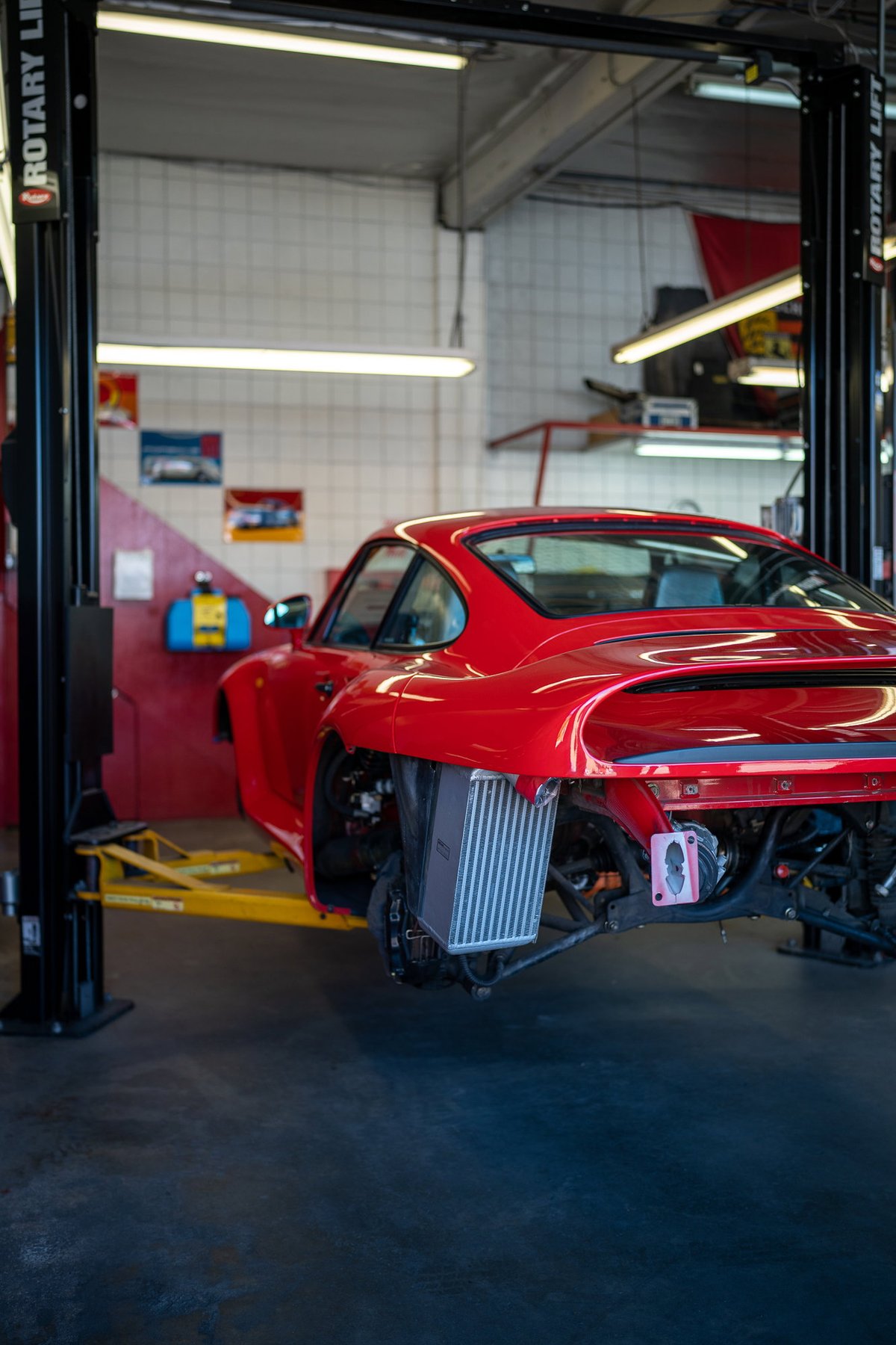 Red Porsche 959 with exposed intercooler, on a lift at a car show.