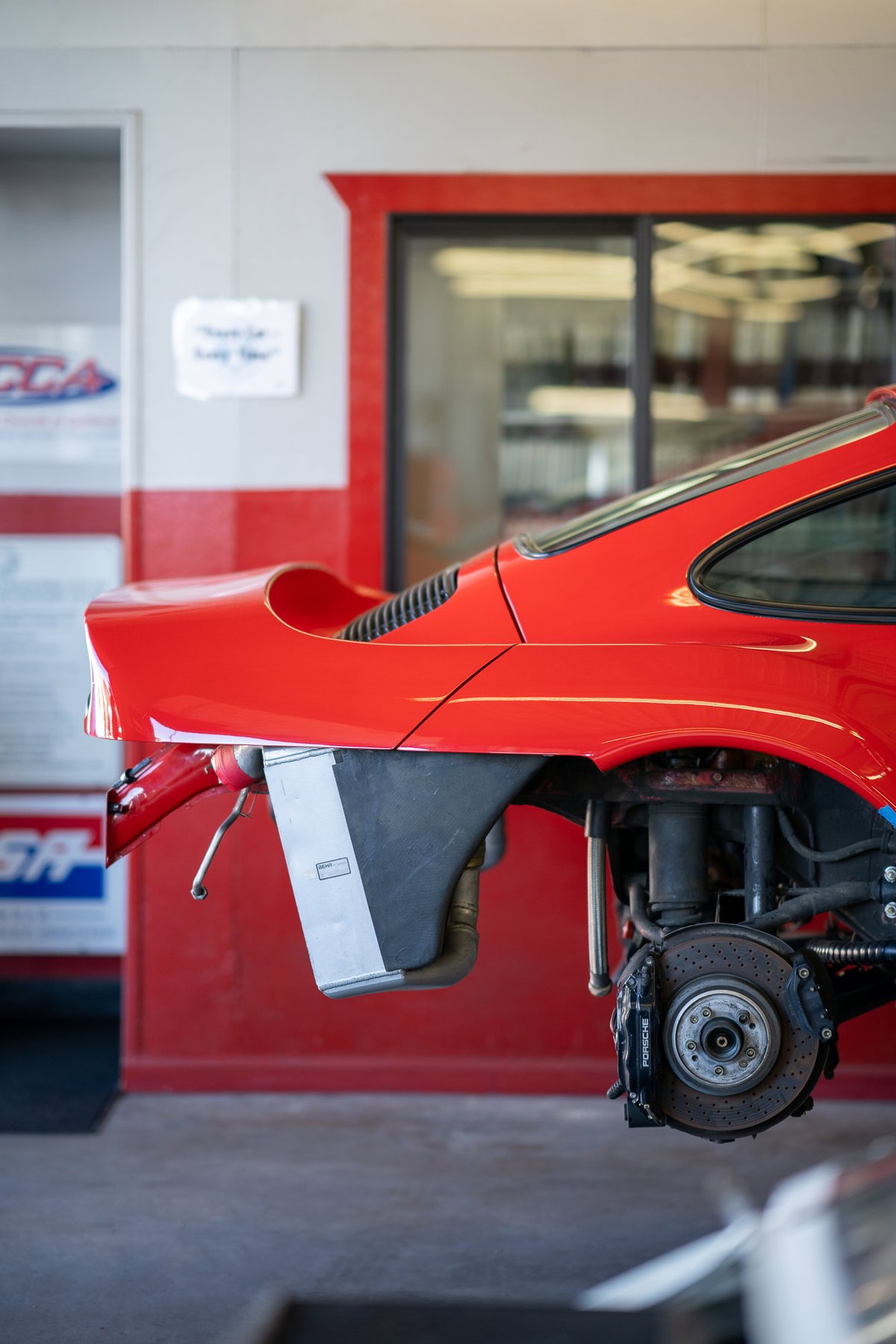 Red Porsche 911 race car rear fender, brake caliper and vented disc rotor detail.