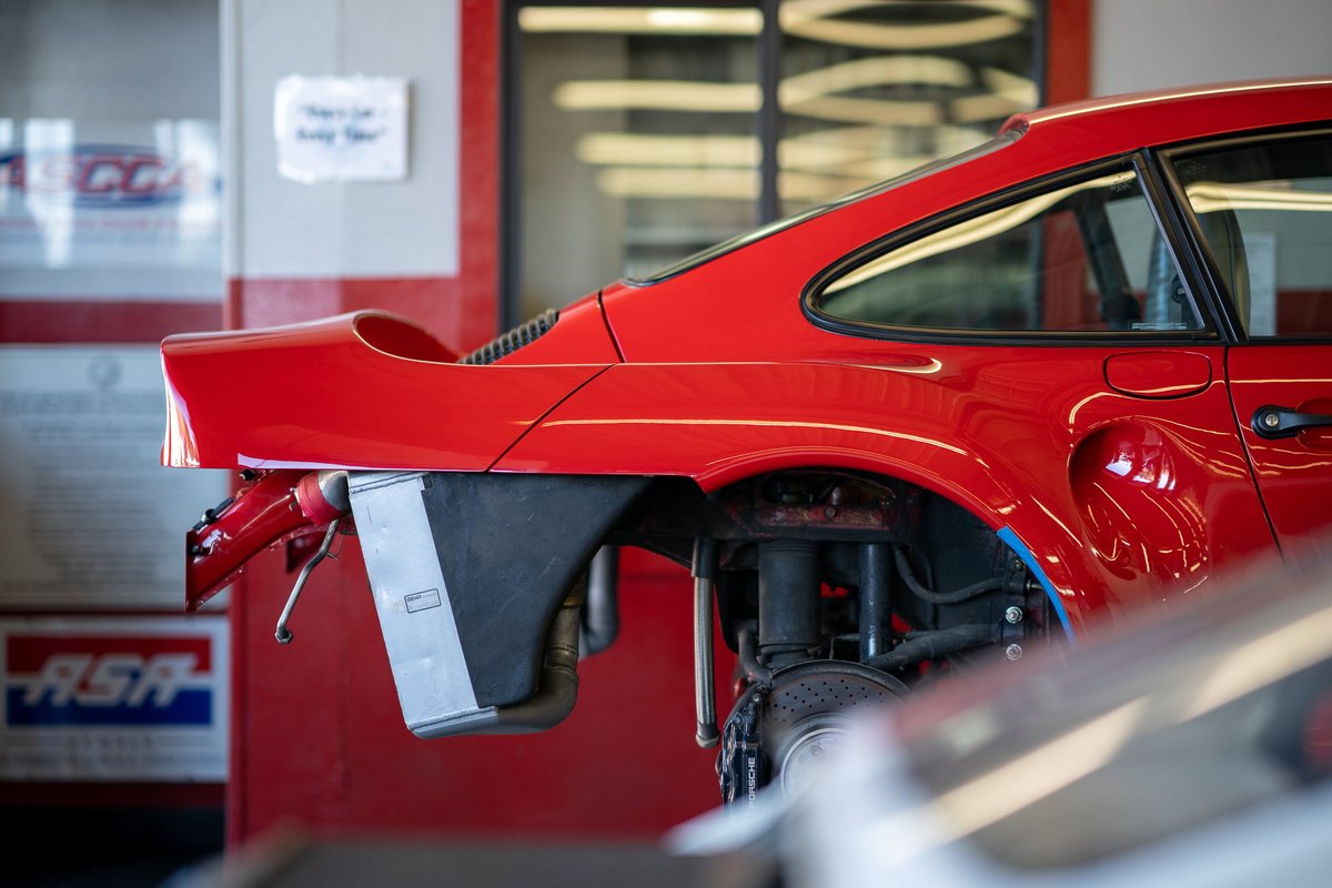 Red Porsche 911 Turbo body panels, trim, and engine bay in a repair shop.