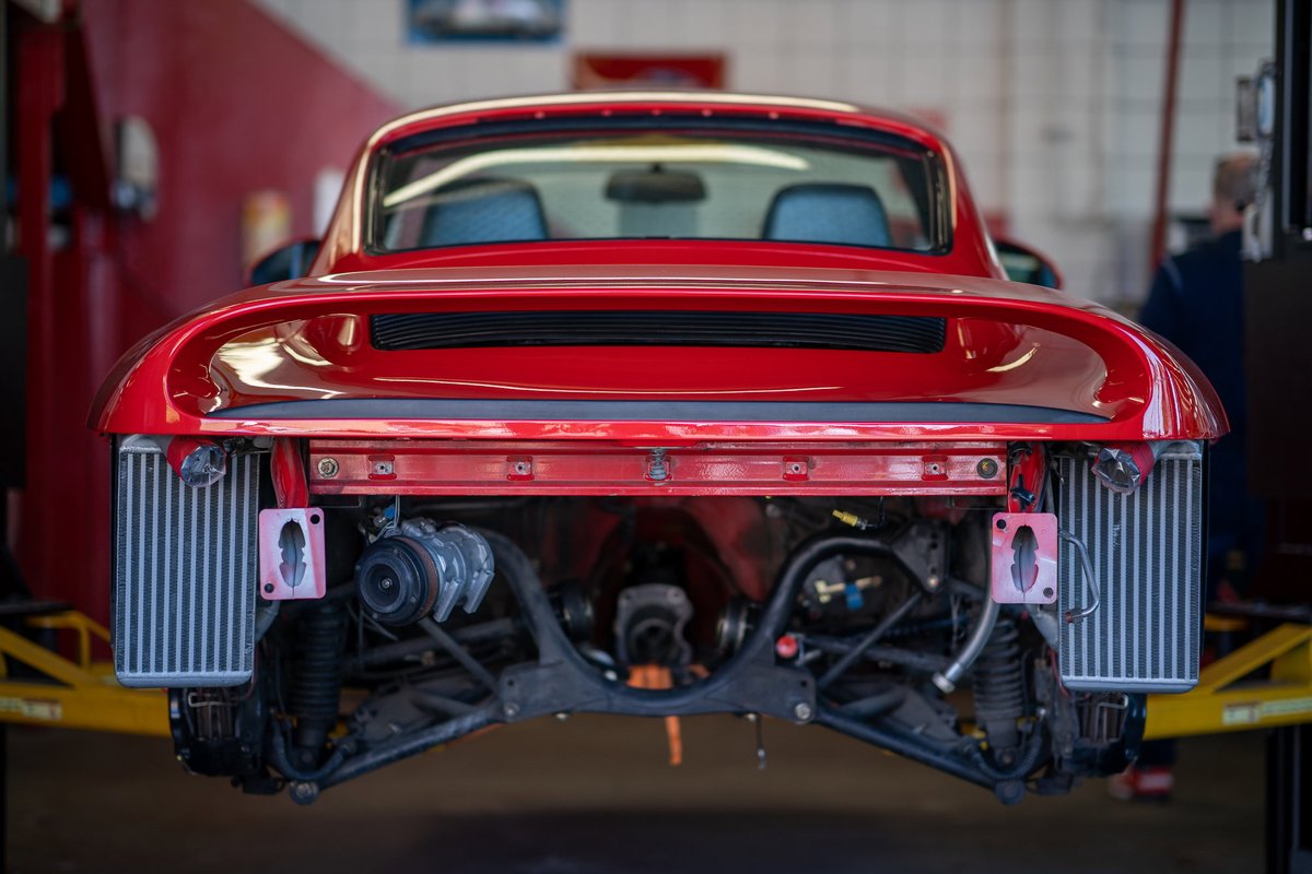 Rear view of a red Porsche 911 undergoing service, with intercoolers visible.