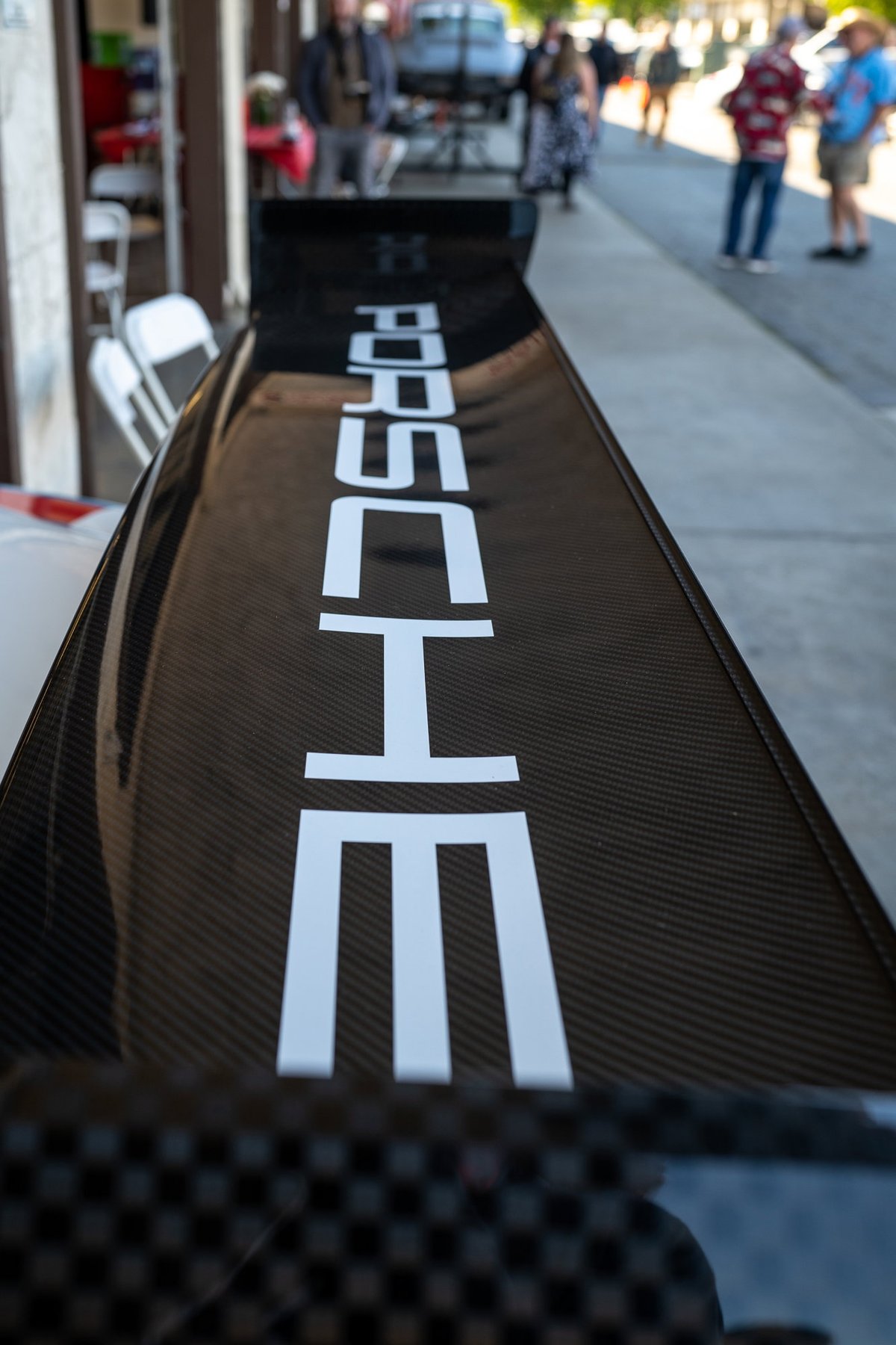 Close-up of a carbon fiber rear spoiler with white "PORSCHE" livery on a black Porsche.