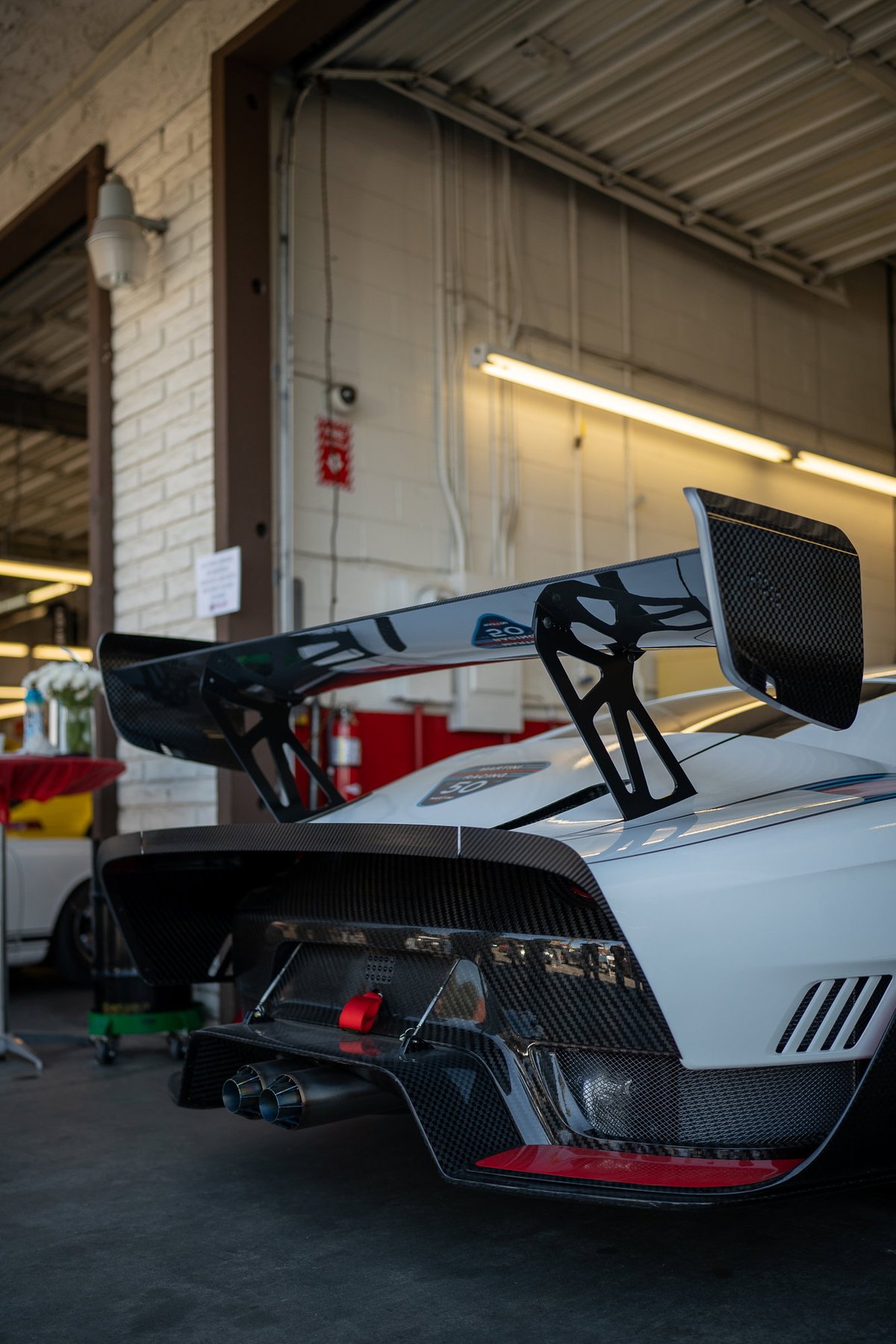 White race car rear: carbon fiber wing, diffuser, and dual exhaust.