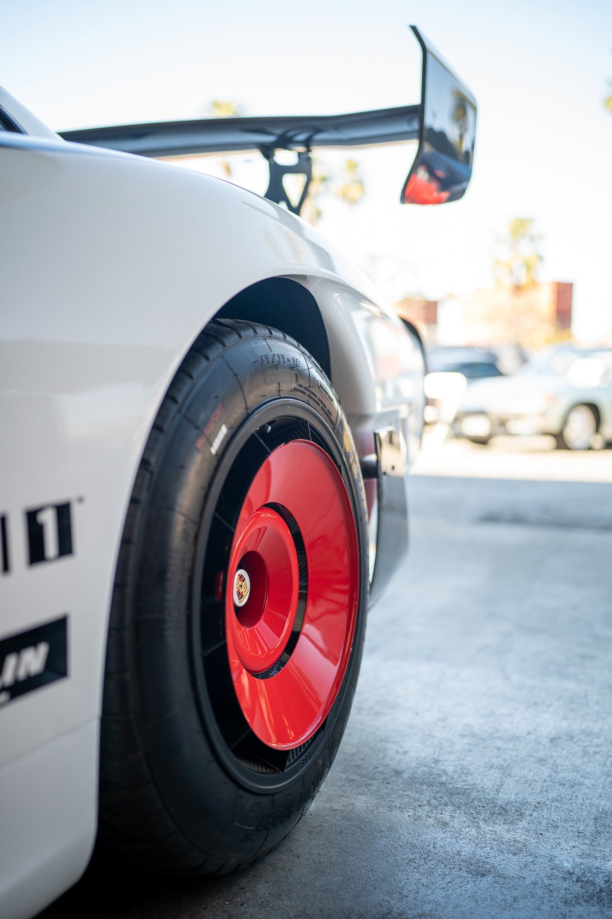Porsche 911 race car with red aero disc rims, black trim, and white livery.