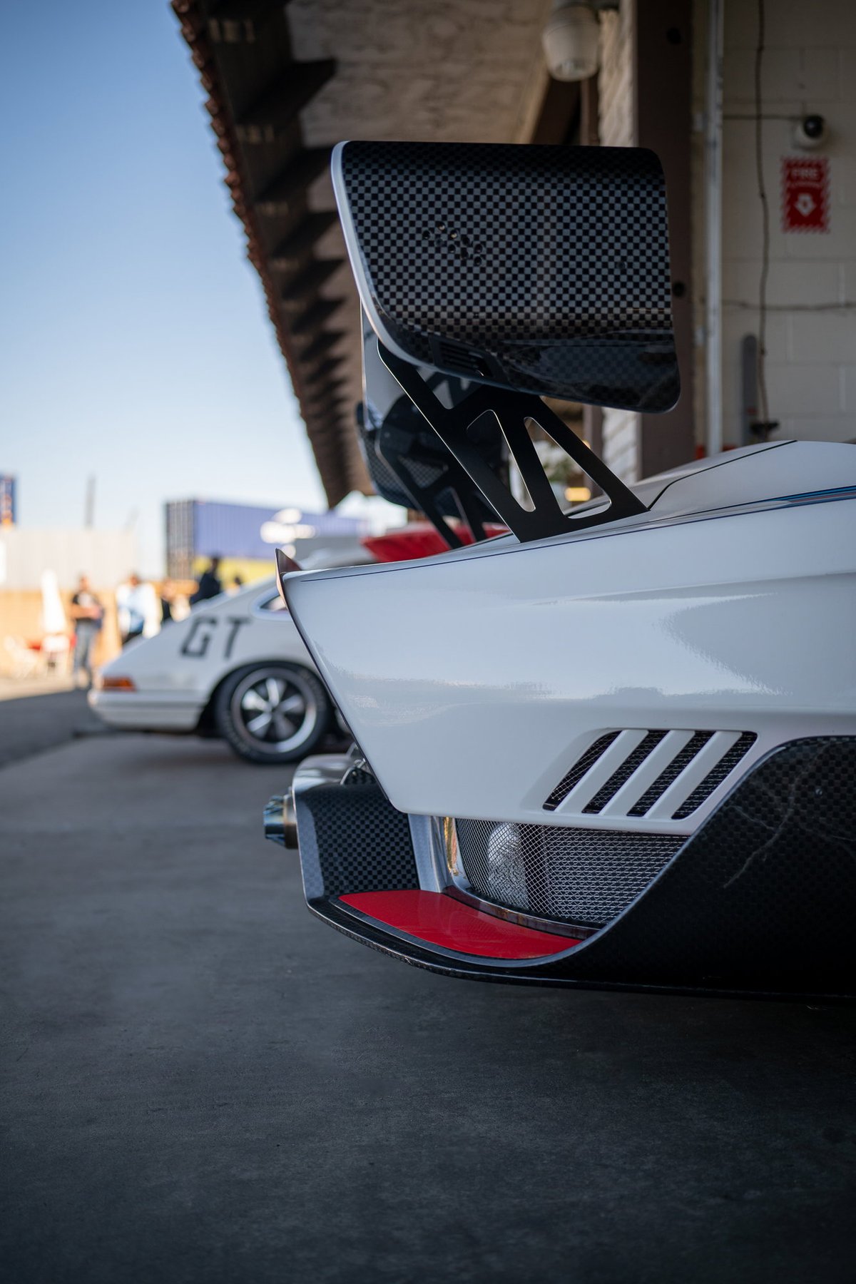 White sports car with carbon fiber wing and red trim.