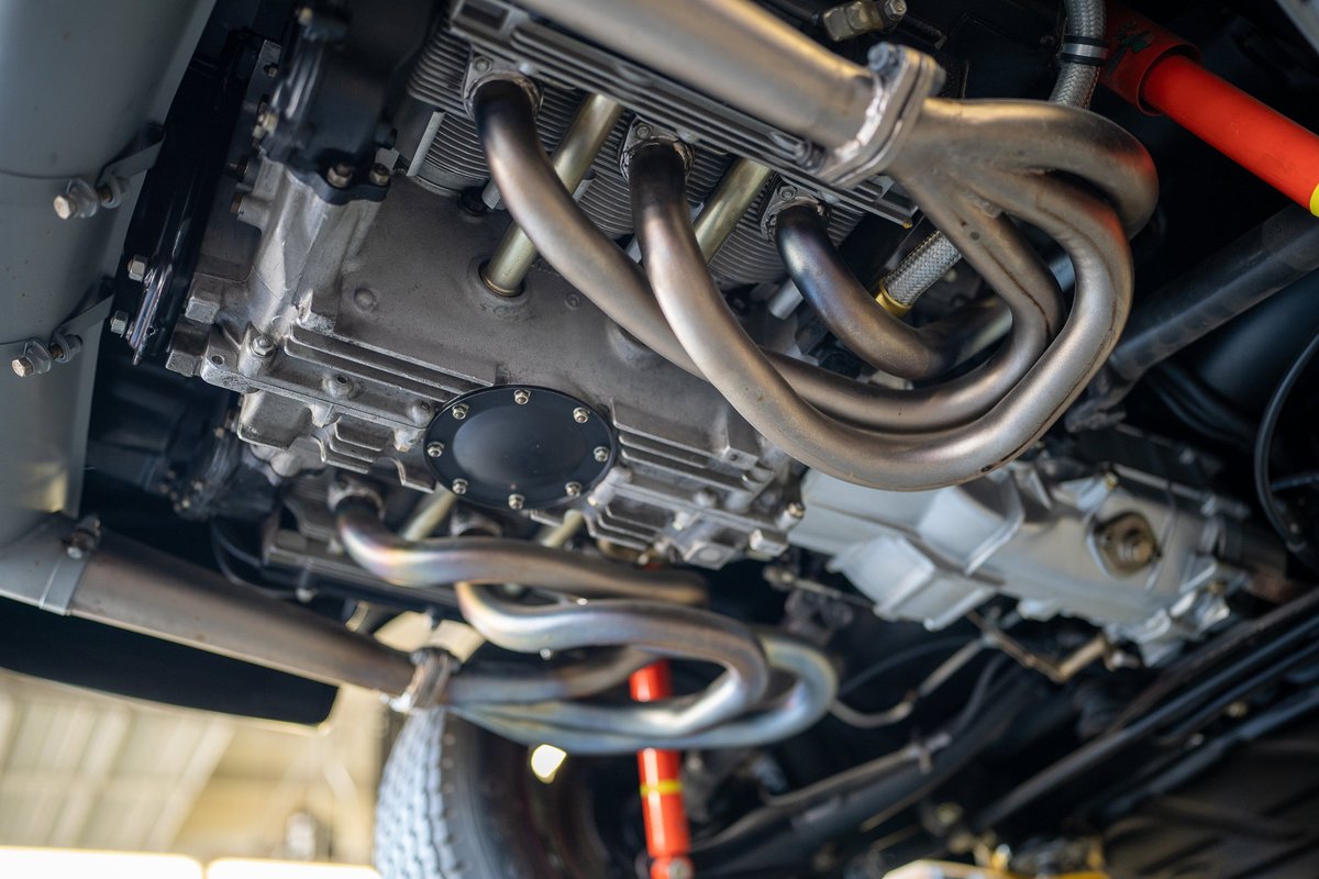 Underneath a vintage Porsche, detailed view of silver flat-six engine with stainless steel exhaust headers.