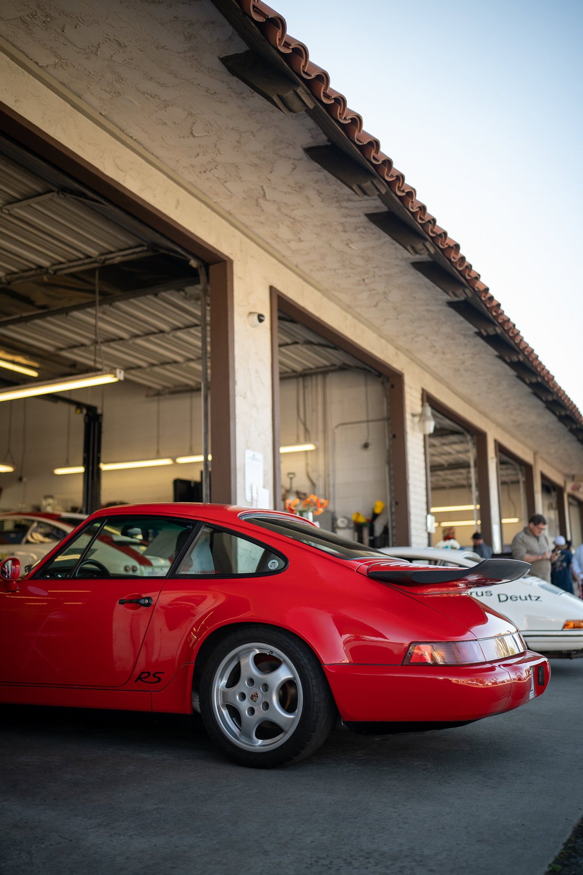 Red Porsche 911 RS with silver Fuchs rims in front of an auto shop.