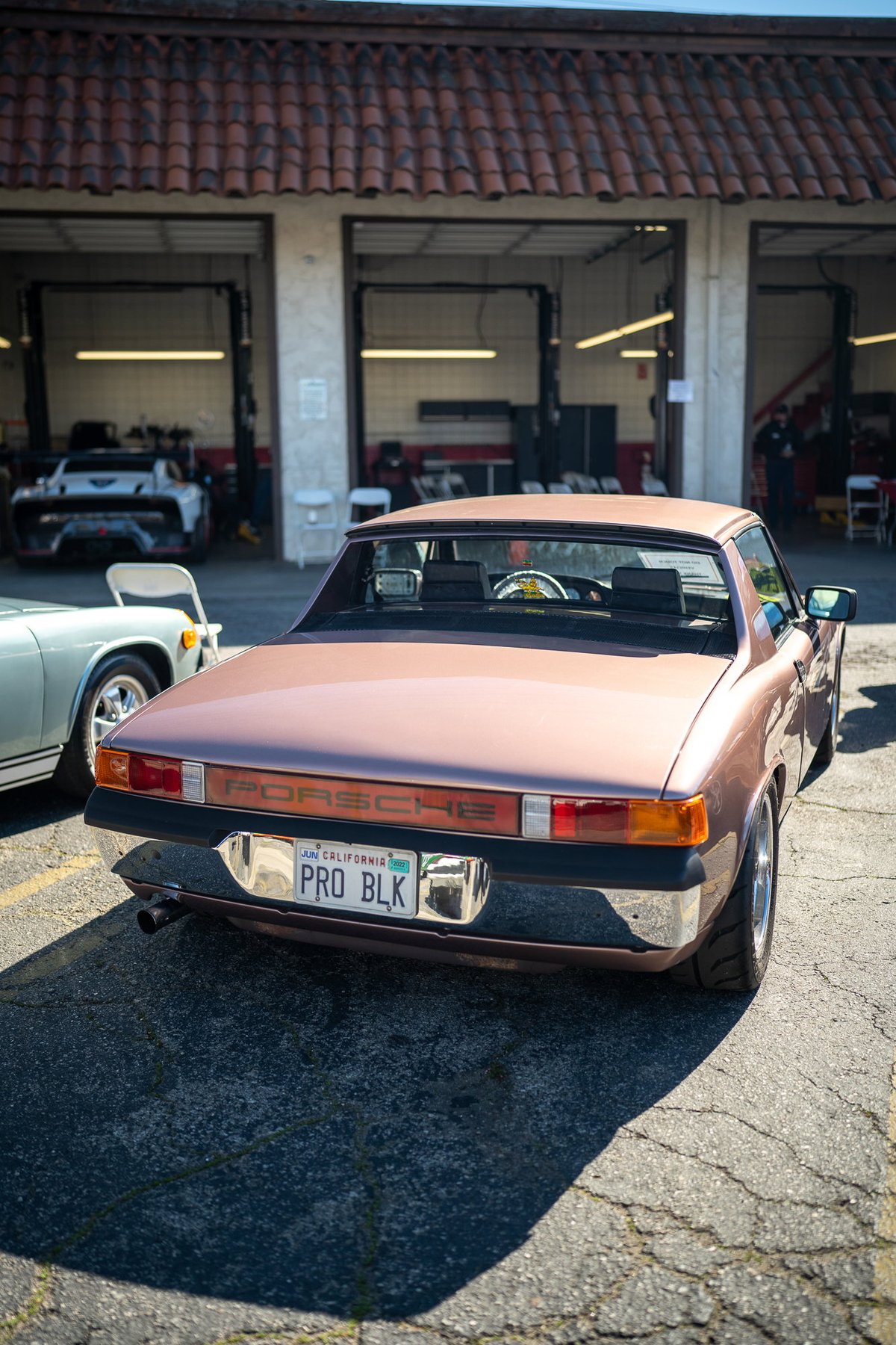 Rear view of a rose gold Porsche 914, parked at a car show in Los Angeles. Chrome bumper and rims.