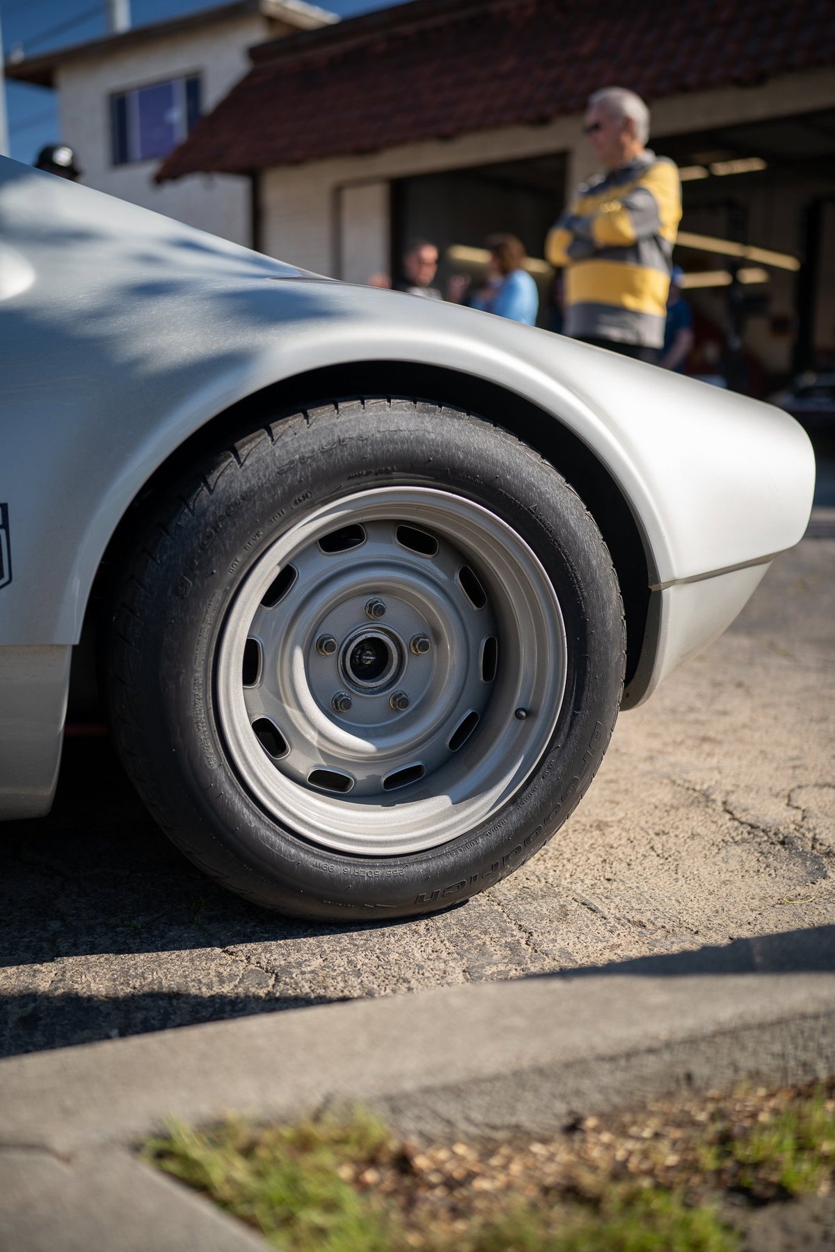 Close-up of a silver vintage race car's rear wheel and fender. The classic steel rim has slotted holes.