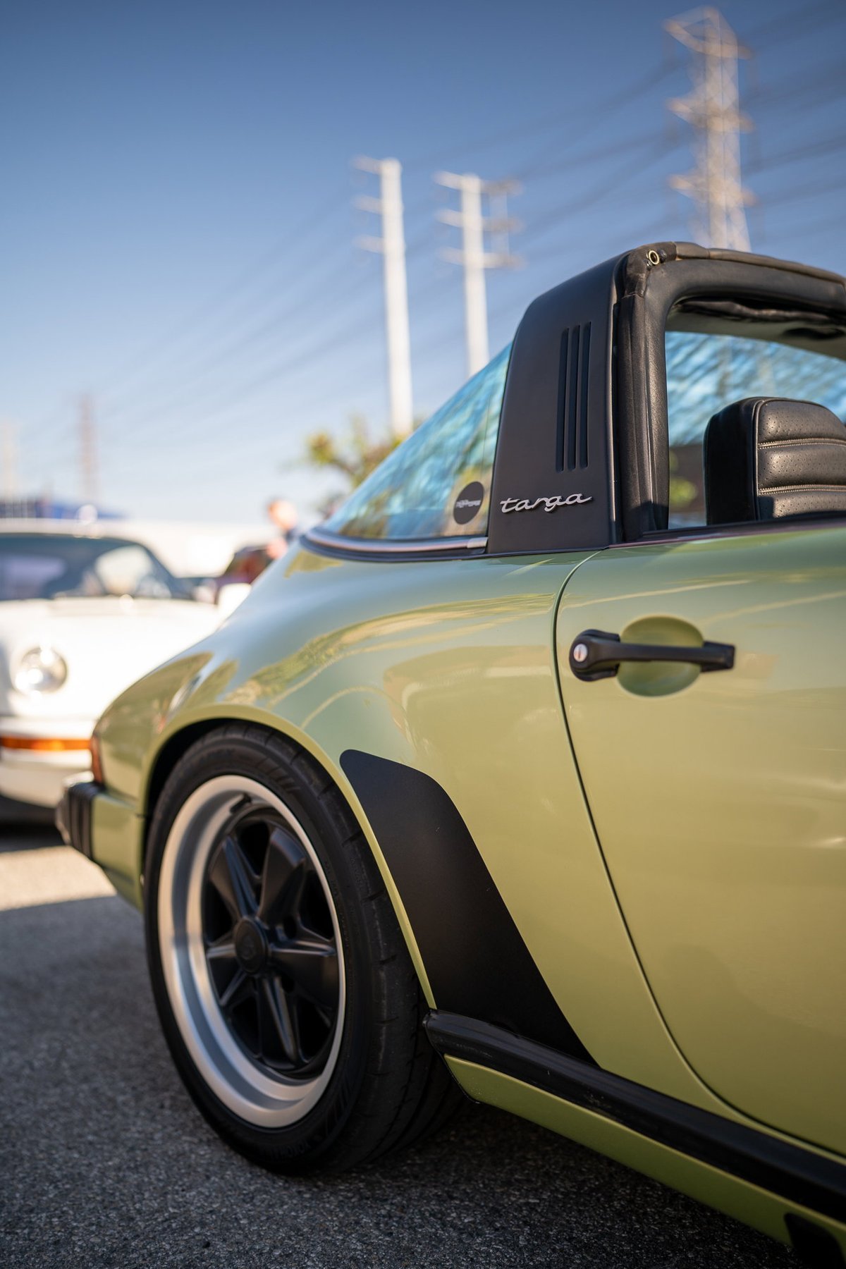 A metallic sage green Porsche 911 Targa with black trim and Fuchs wheels.