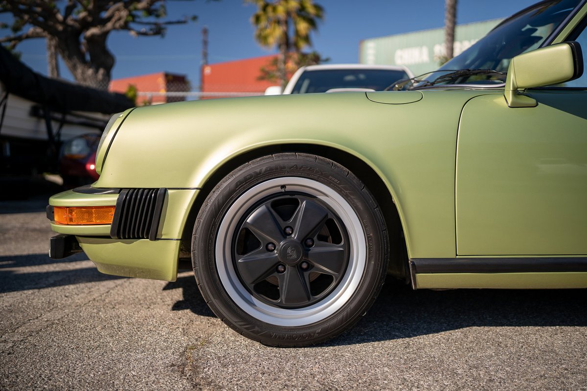 Front fender of a light green Porsche 911 showing its black Fuchs rims.