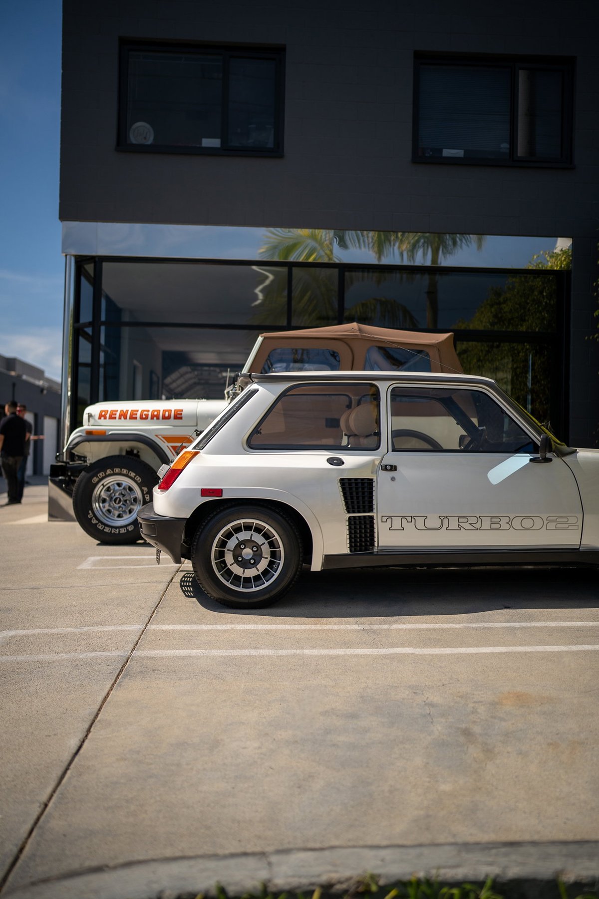 White Renault 5 Turbo 2 with "TURBO 2" side trim, parked next to a Jeep Renegade.