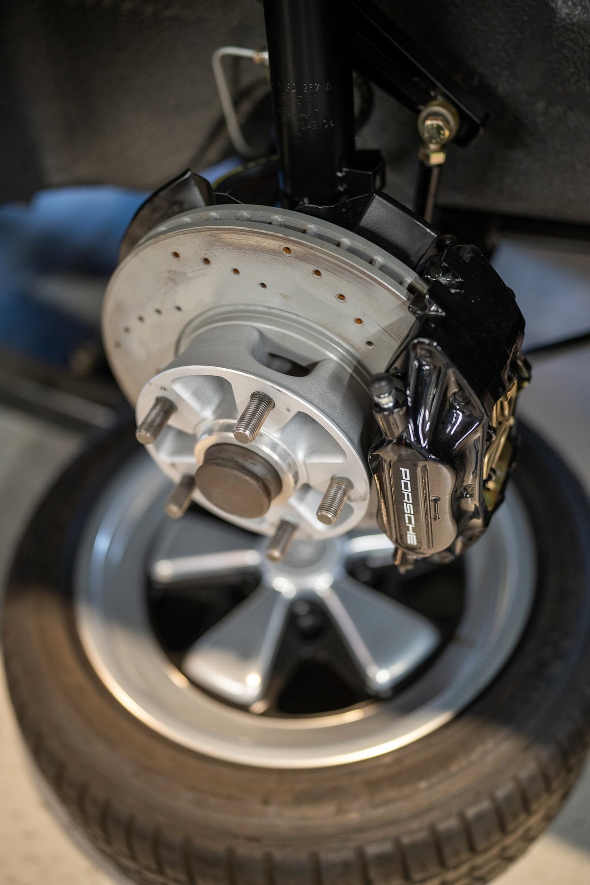 Close up of a Porsche brake caliper with slotted rotor and Fuchs rim.