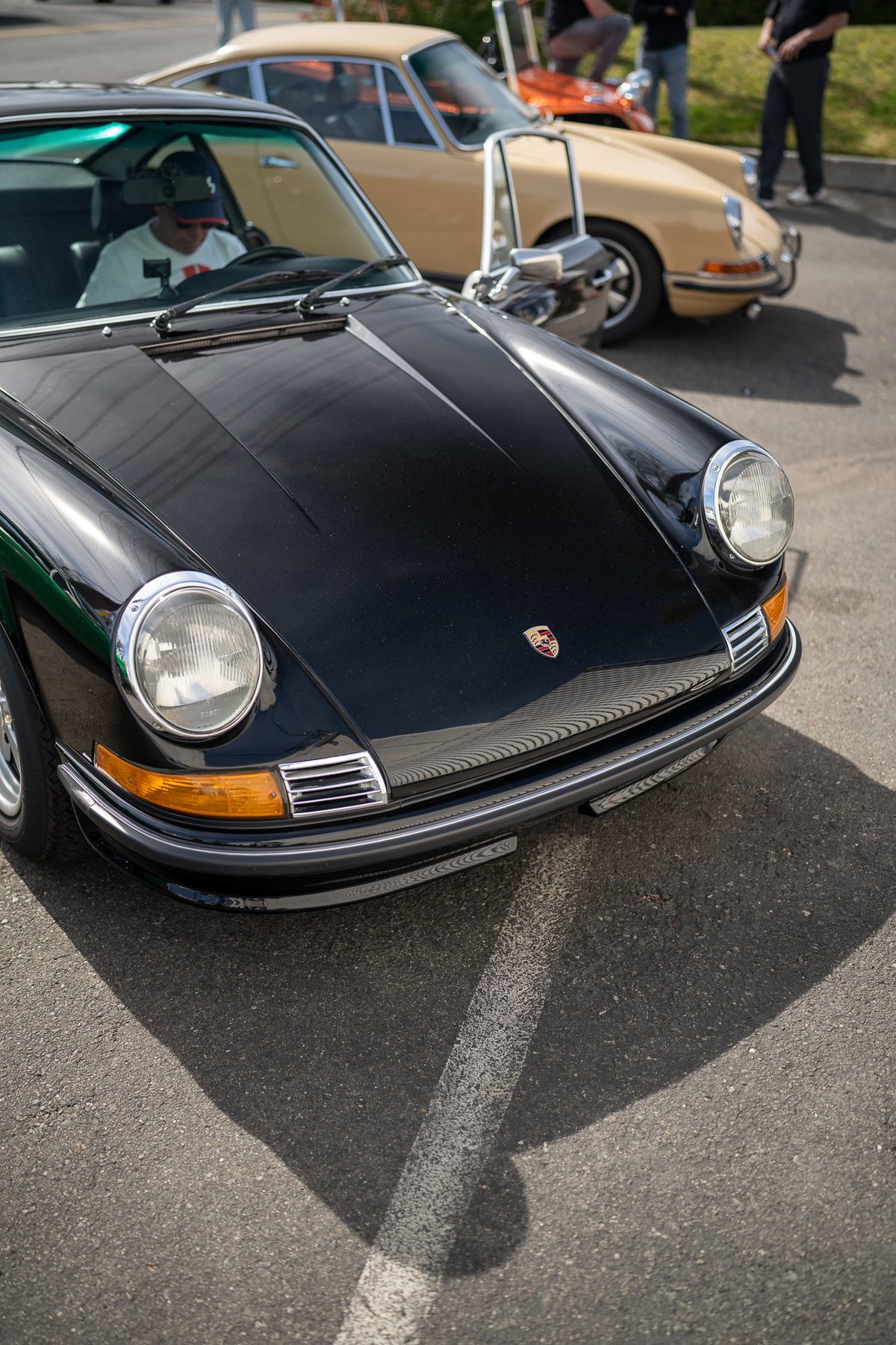 Front view of a black Porsche 911 with chrome trim and a yellowed tan Porsche 911 in the background.
