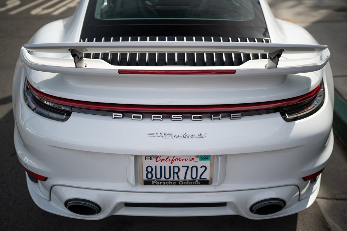 White Porsche 911 Turbo S rear with a large wing and quad exhaust tips.