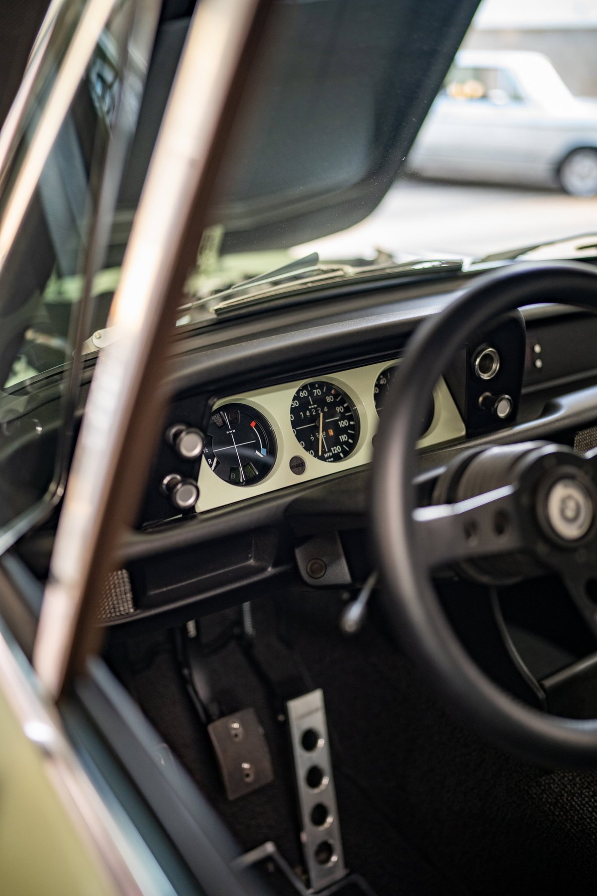 Interior view of a vintage BMW 2002 with classic gauges, sport steering wheel, and floor-mounted pedals.