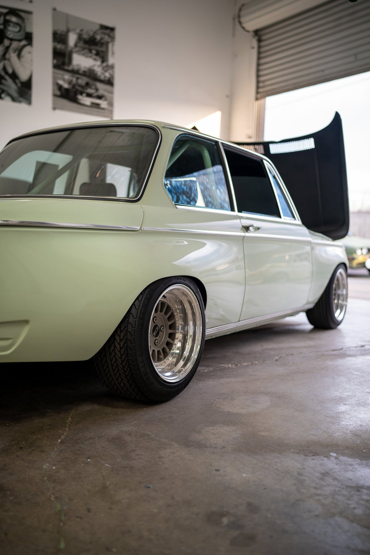 Low-angle shot of a vintage mint green BMW 2002 with polished chrome rims and wide tires.