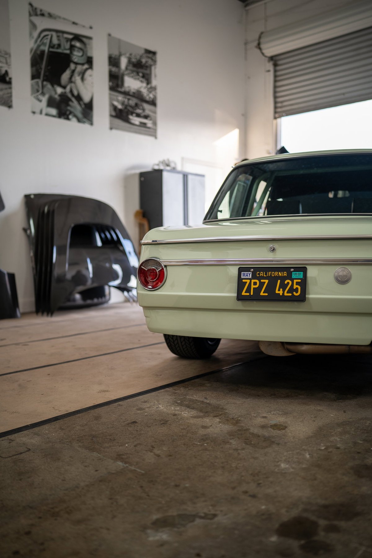 Rear of a light green 1970s BMW 2002 with California plates in a garage.