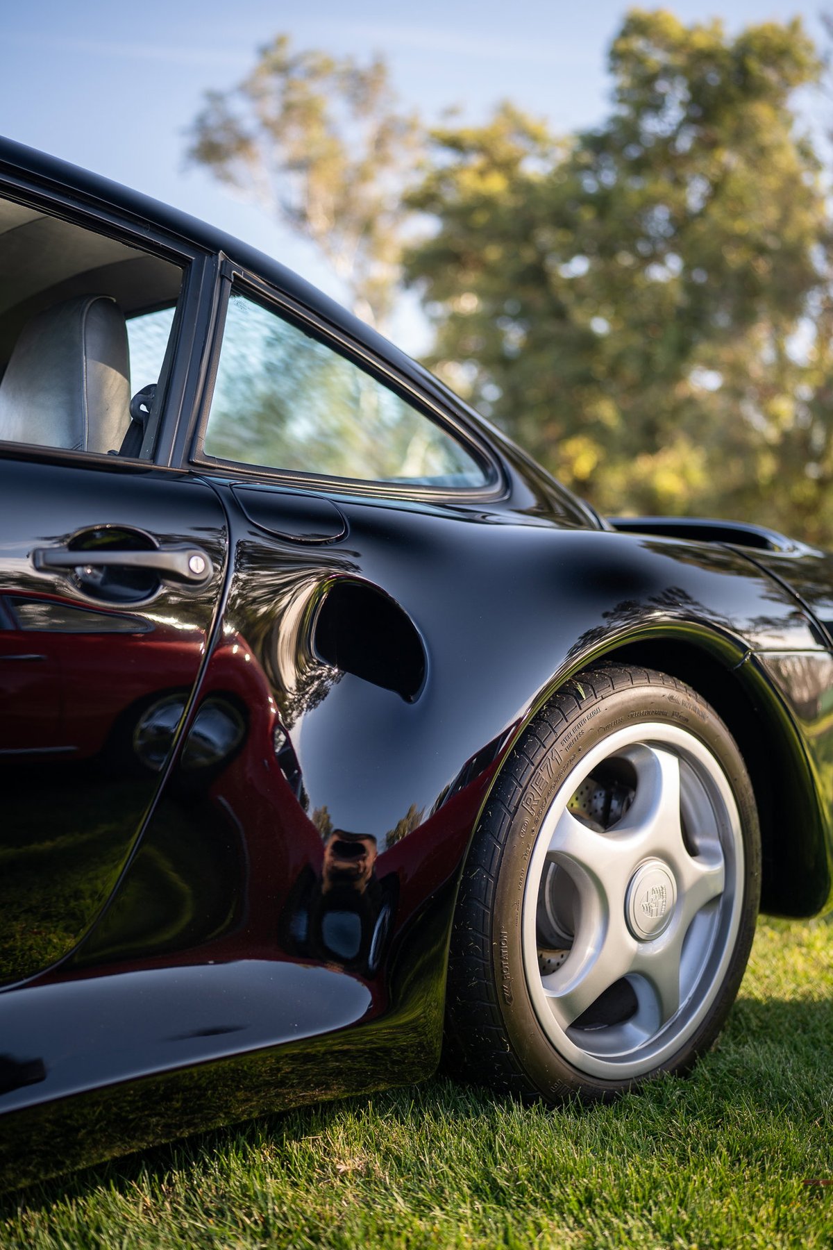 Black Porsche 959 with five-spoke alloy rims, parked on grass.
