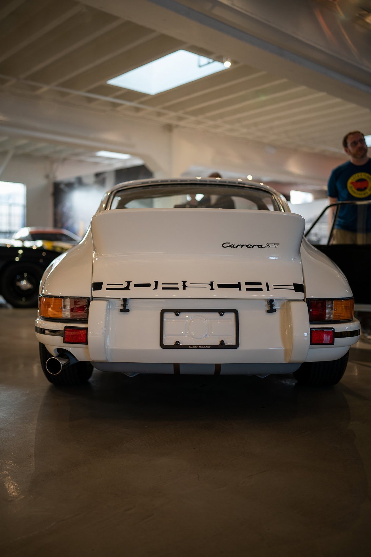 Rear view of a white 1973 Porsche 911 Carrera RS with black trim and a chrome exhaust pipe.