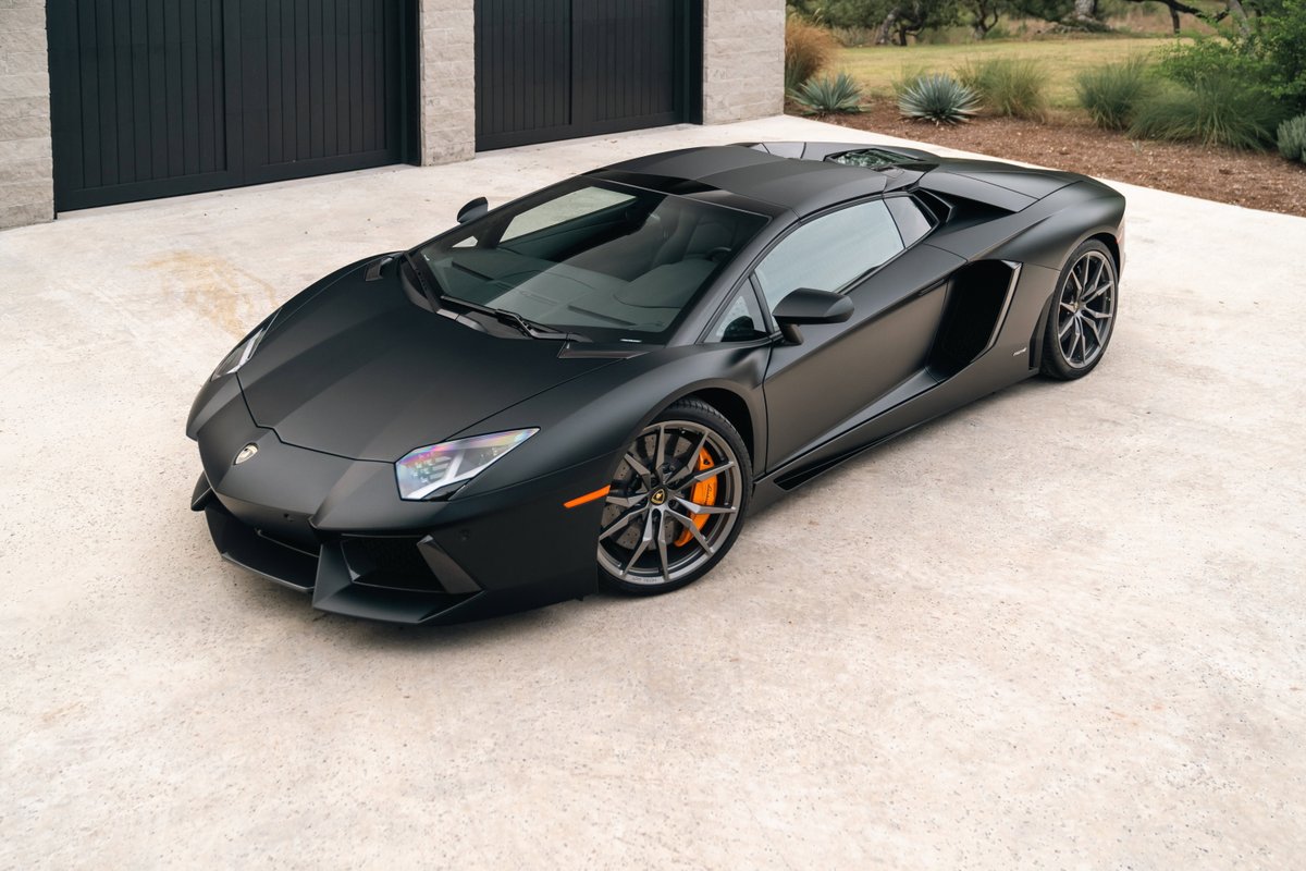 Matte black Lamborghini Aventador LP700-4 with orange brake calipers and grey rims.