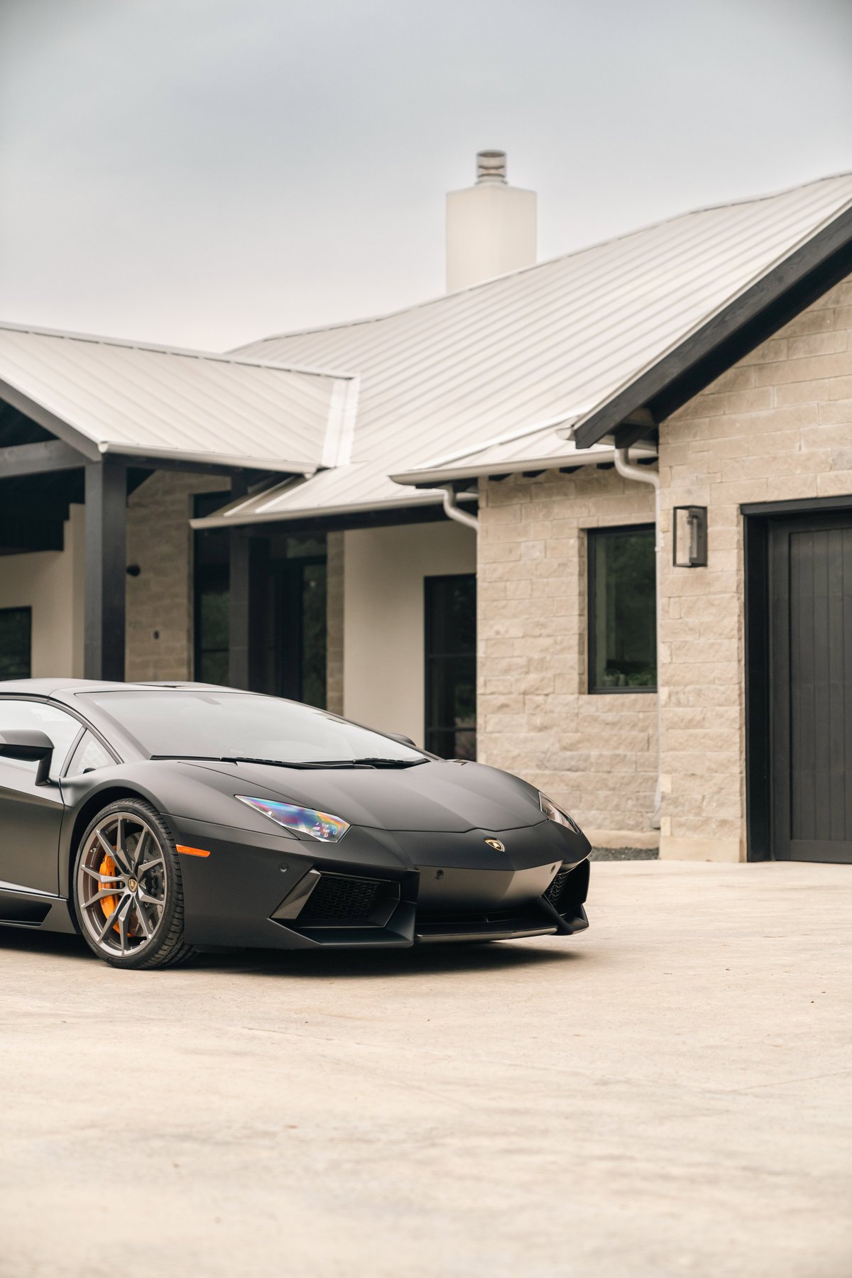 Matte black Lamborghini Aventador LP700-4 with orange brake calipers and silver multi-spoke rims.