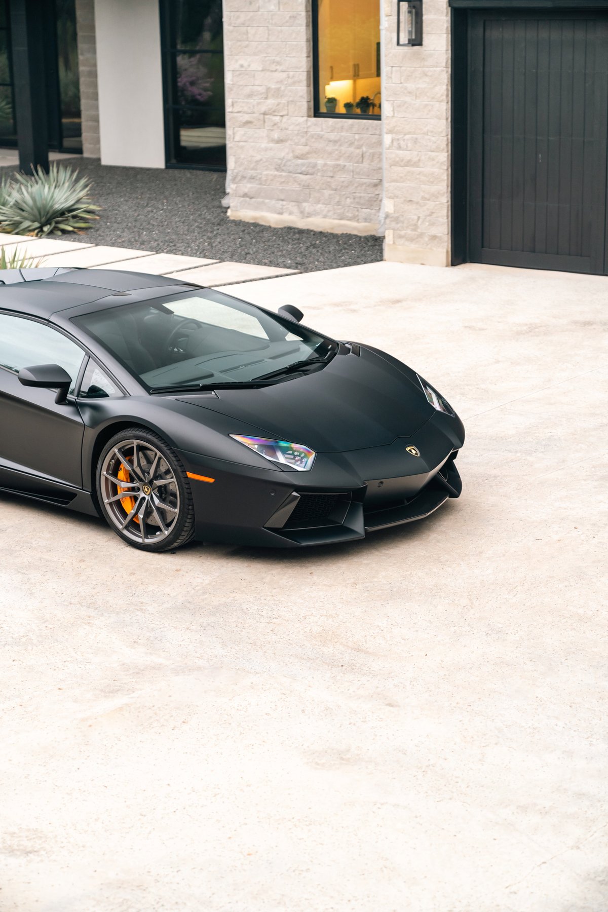 Matte black Lamborghini Aventador LP700-4 with orange brake calipers and grey multi-spoke rims.