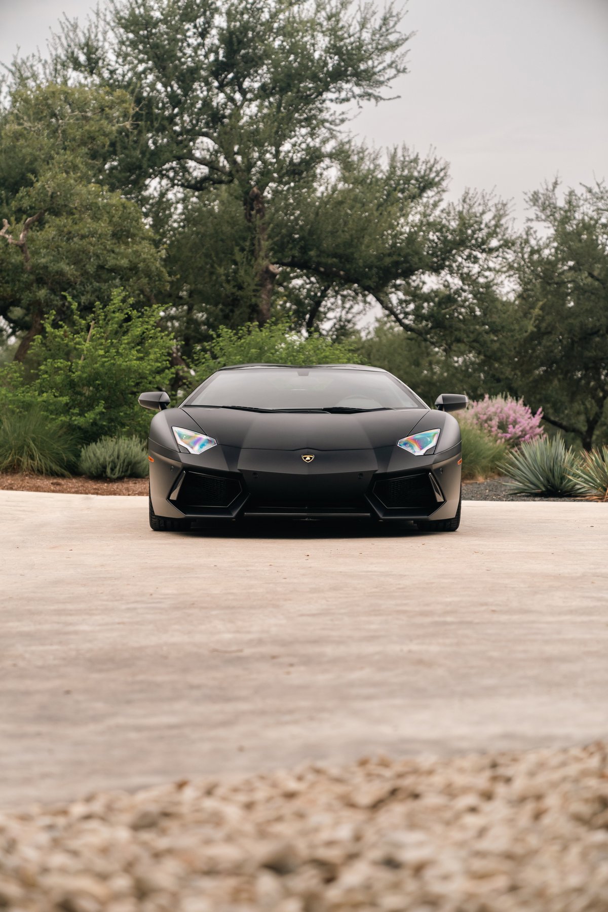 Matte black Lamborghini Aventador LP700-4 front view with iridescent headlights.