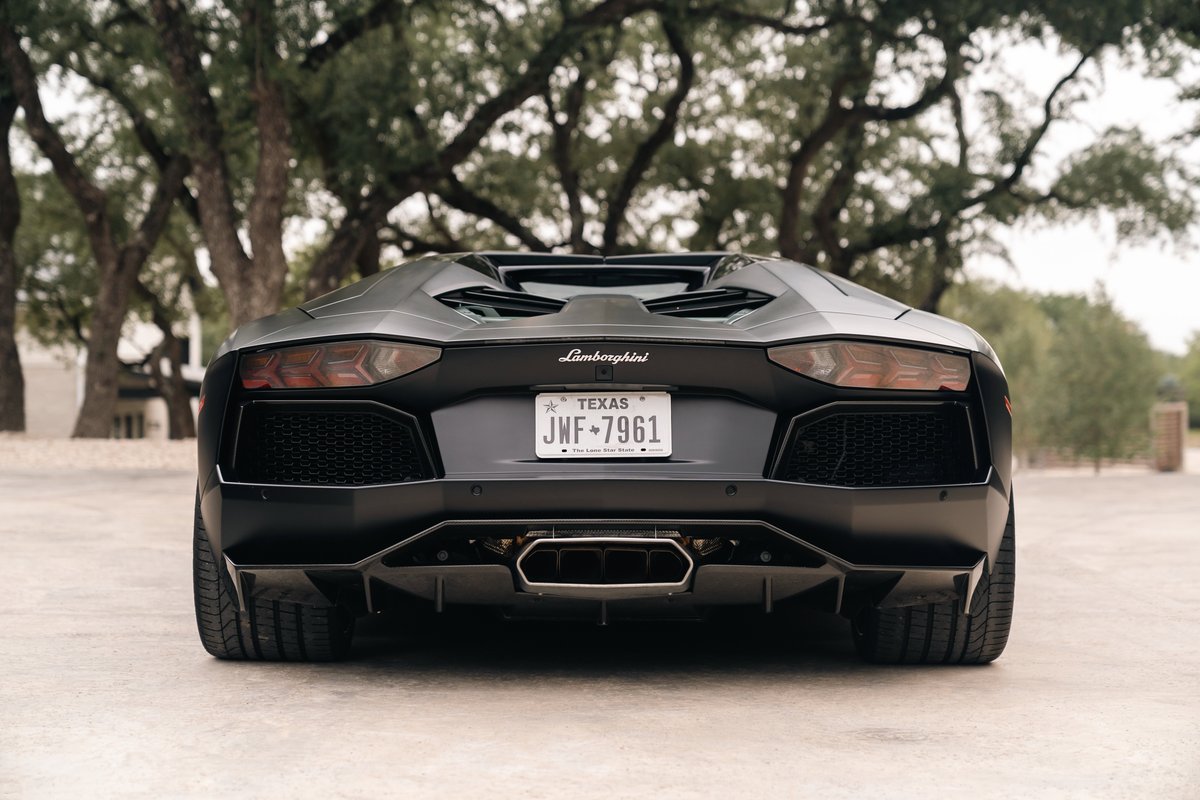 Matte black Lamborghini Aventador LP700-4 rear view, showing quad exhaust and sharp diffuser.