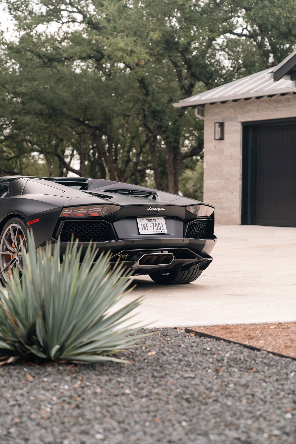 Matte black Lamborghini Aventador LP700-4 rear view, with orange brake calipers and aggressive exhaust tips.